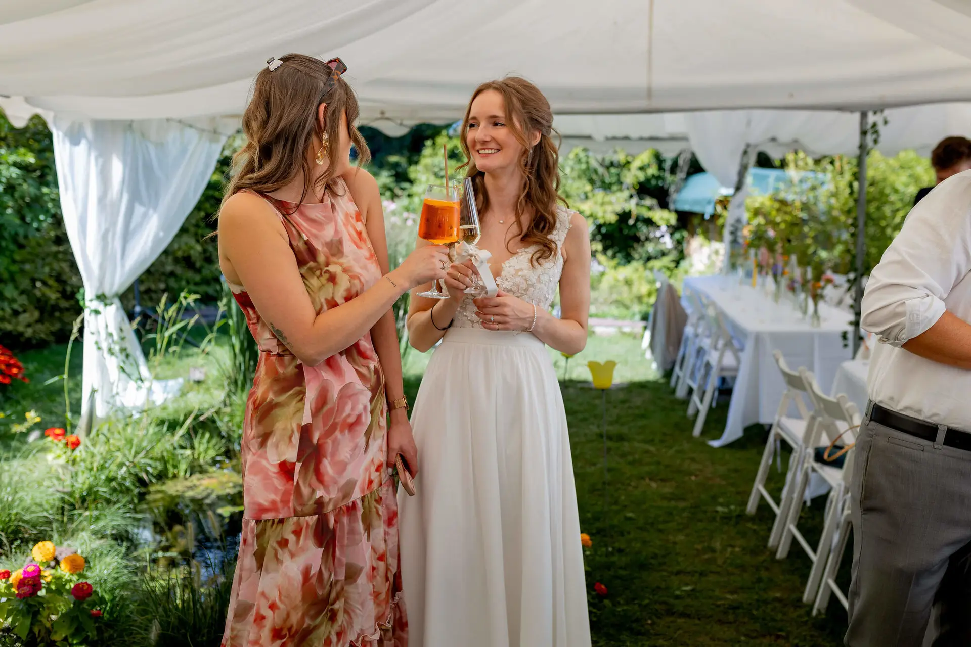 Braut stößt mit einer Freundin mit Cocktails im Garten an