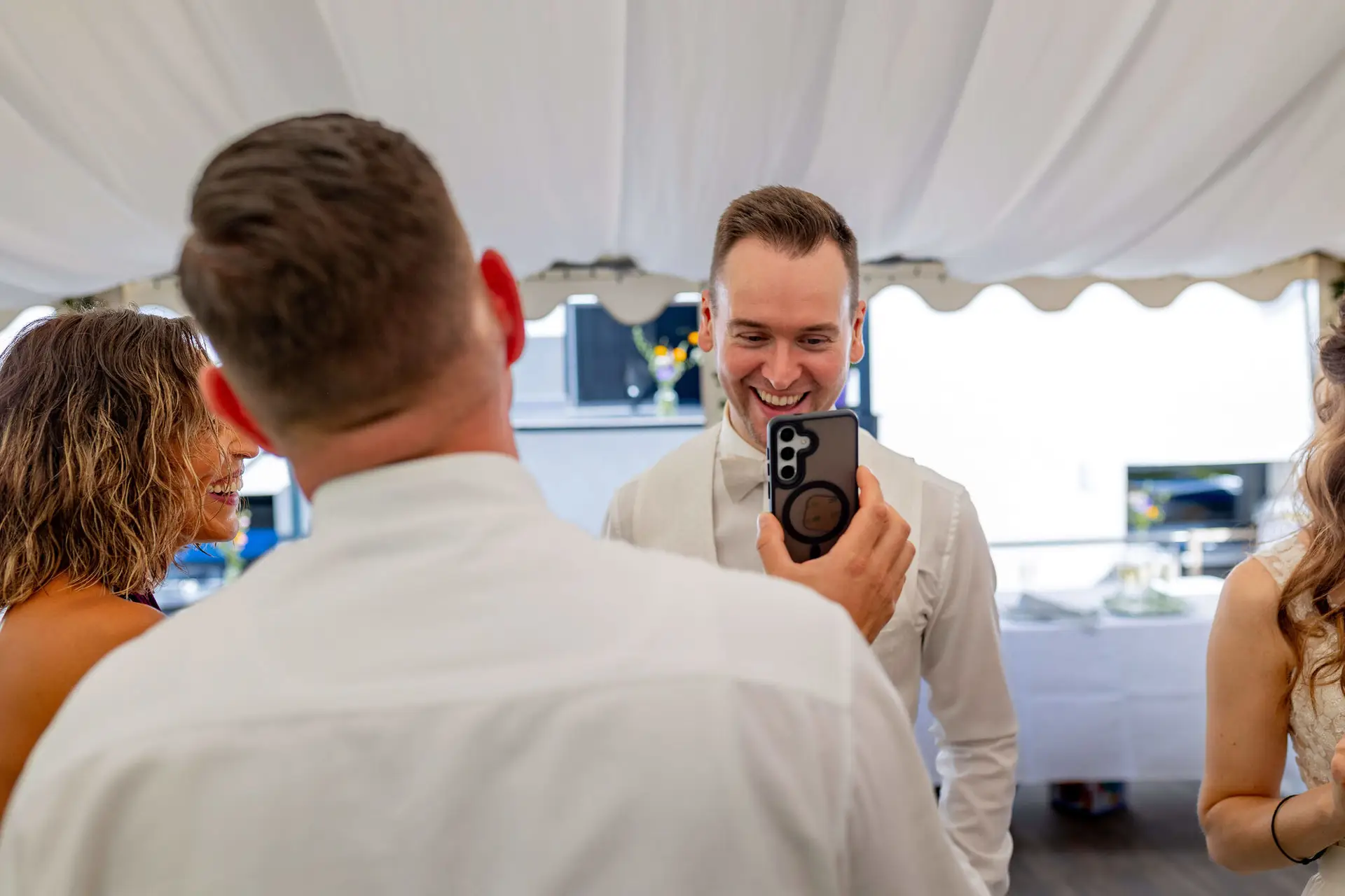 Bräutigam zeigt lachend ein Foto auf dem Handy bei der Gartenparty