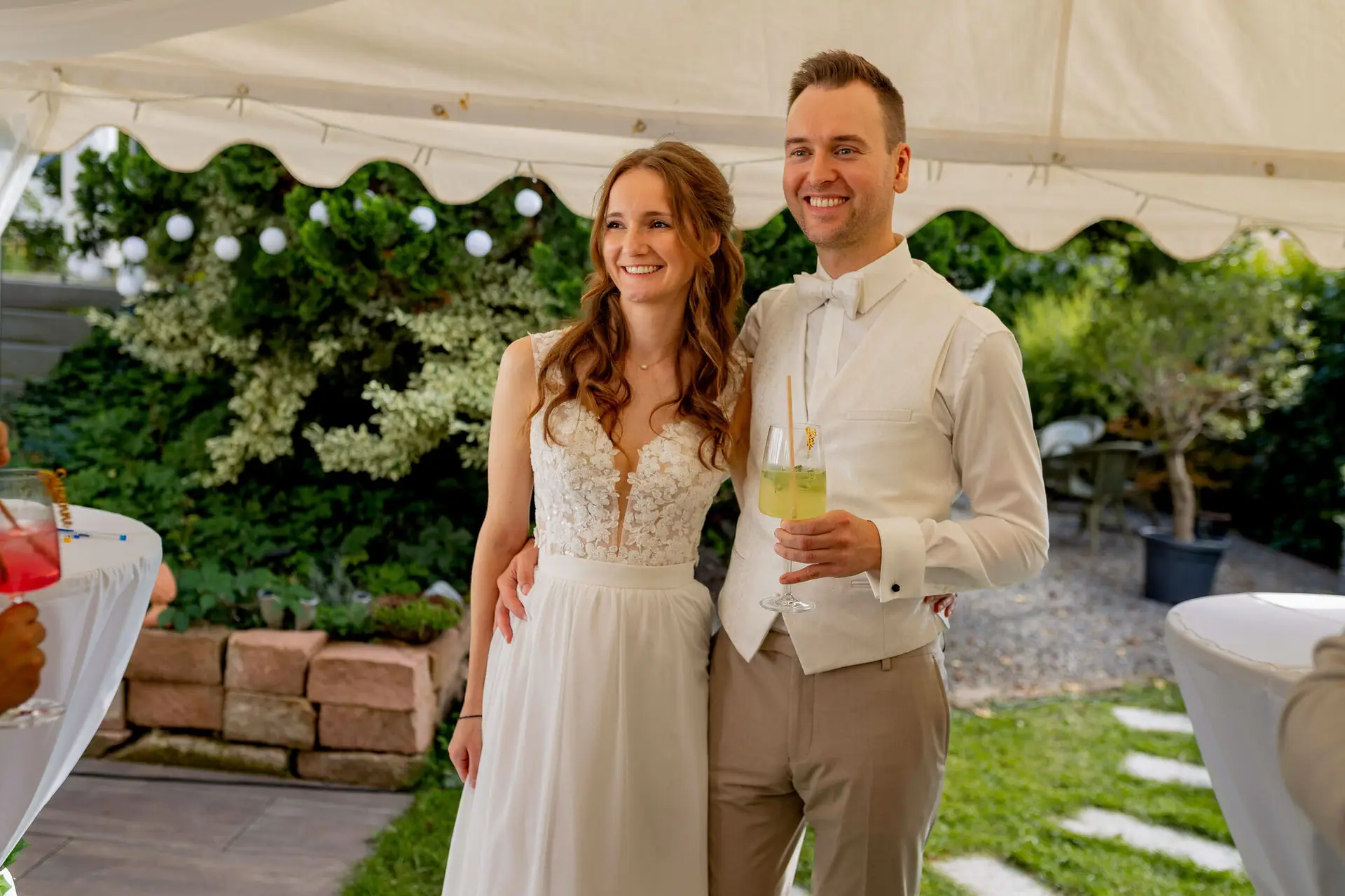Brautpaar lächelt in die Kamera mit Cocktails bei der Gartenparty