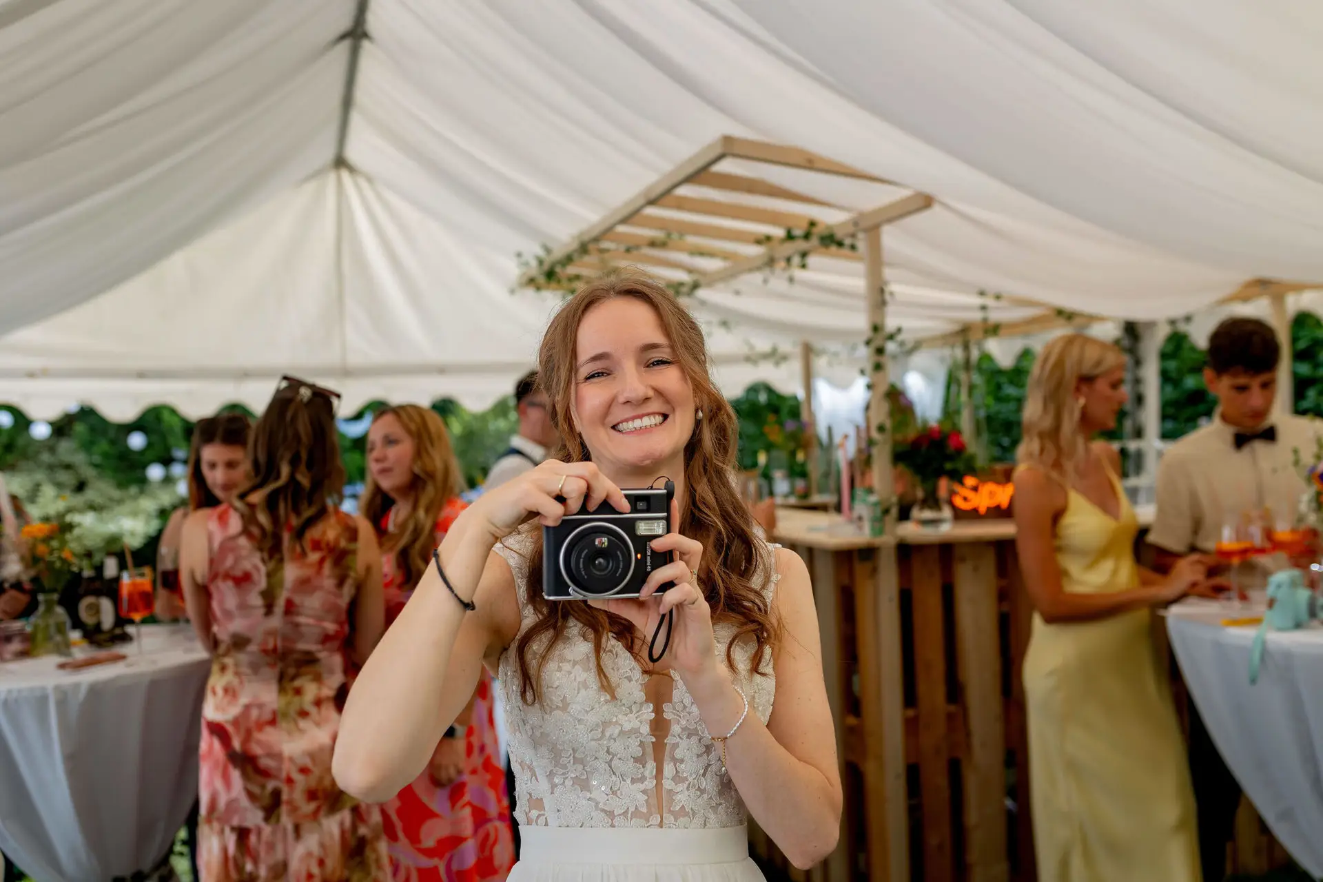 Braut hält lächelnd eine Instax-Kamera im geschmückten Zelt