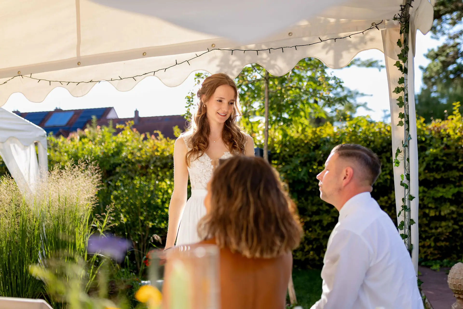 Braut steht lächelnd im Abendlicht unter dem Gartenzelt