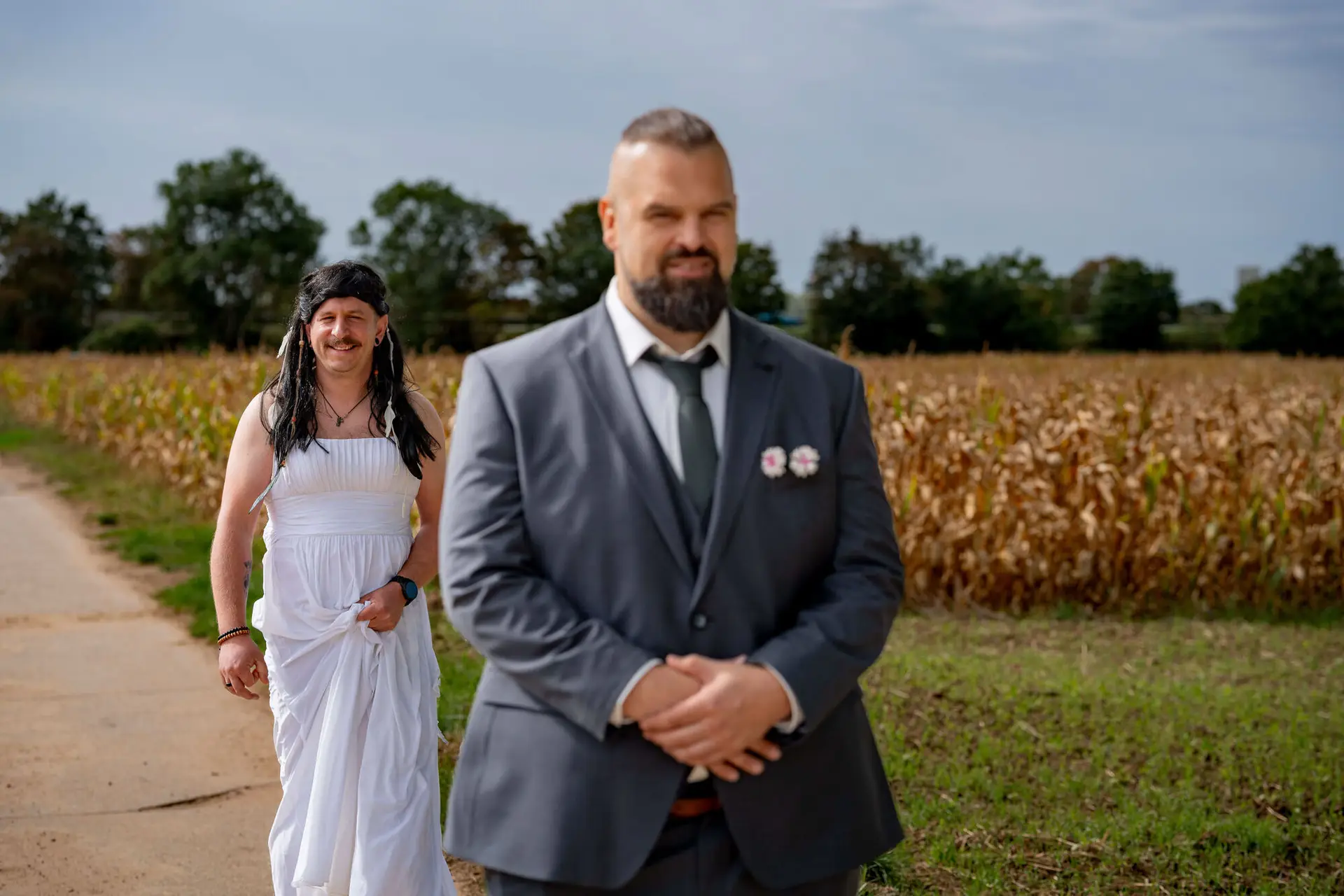 Freund im weißen Kleid mit Perücke schleicht sich von hinten an den wartenden Bräutigam heran