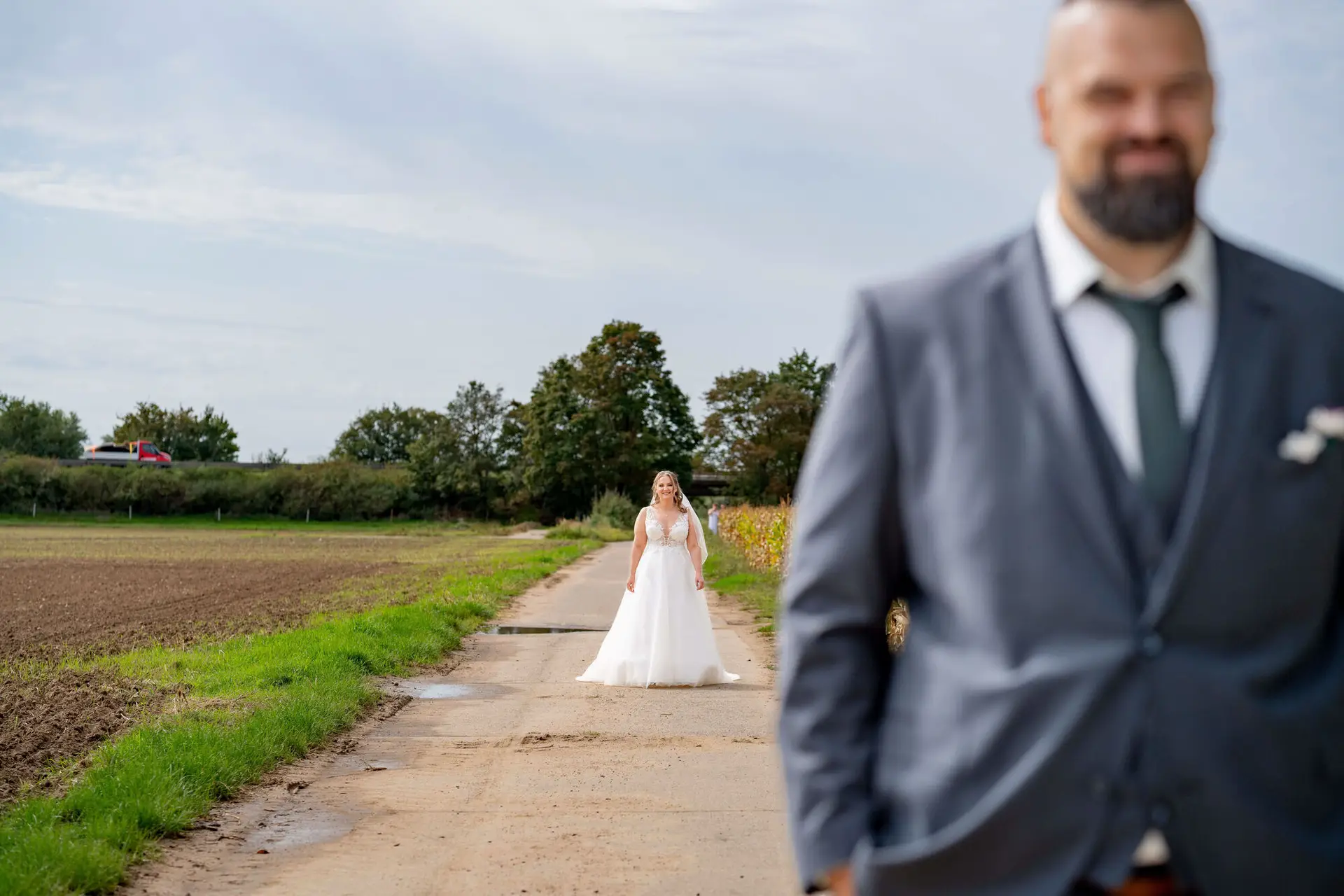 Braut im Brautkleid nähert sich dem wartenden Bräutigam auf dem Feldweg