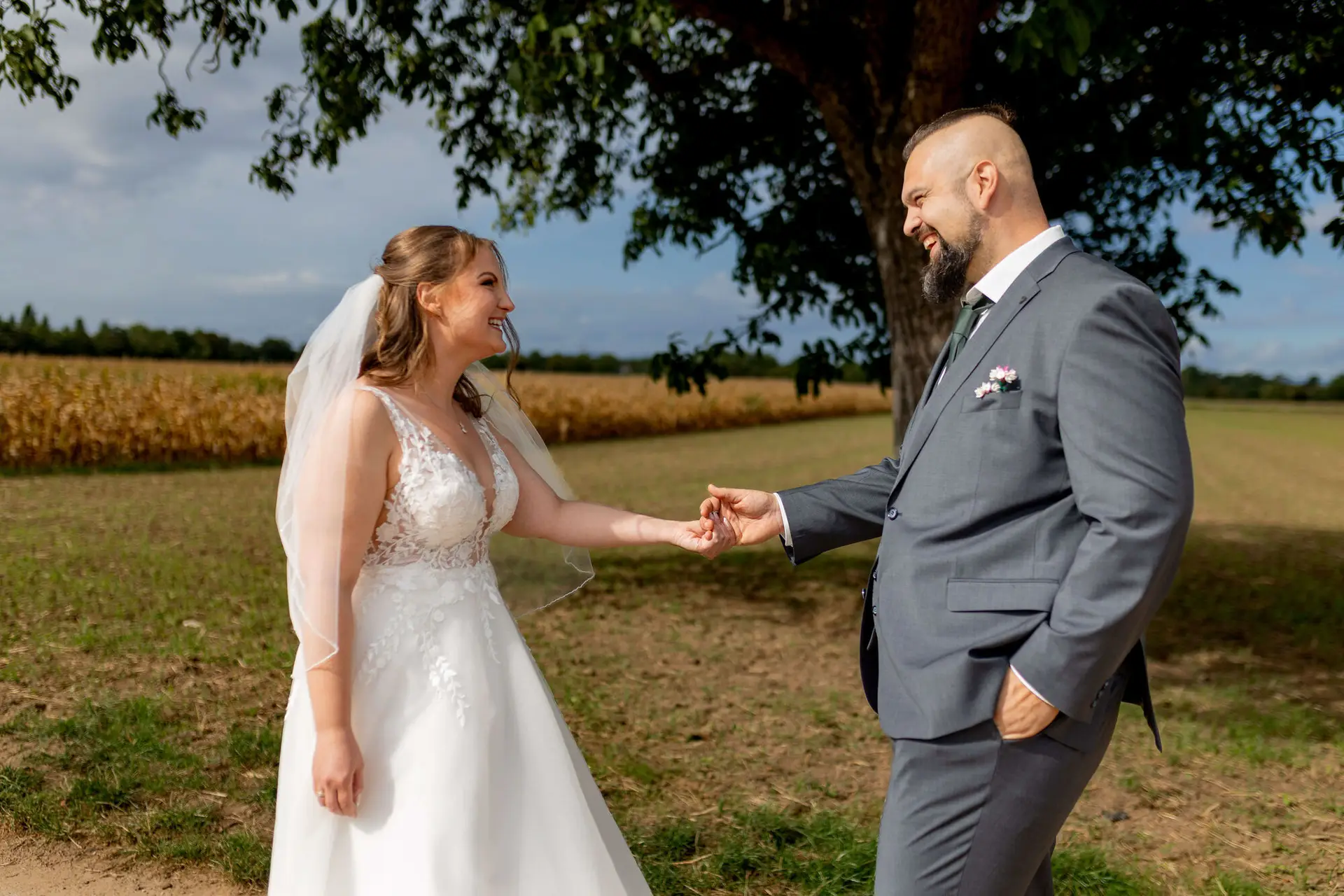 Brautpaar hält Händchen und lächelt sich an unter einem Baum