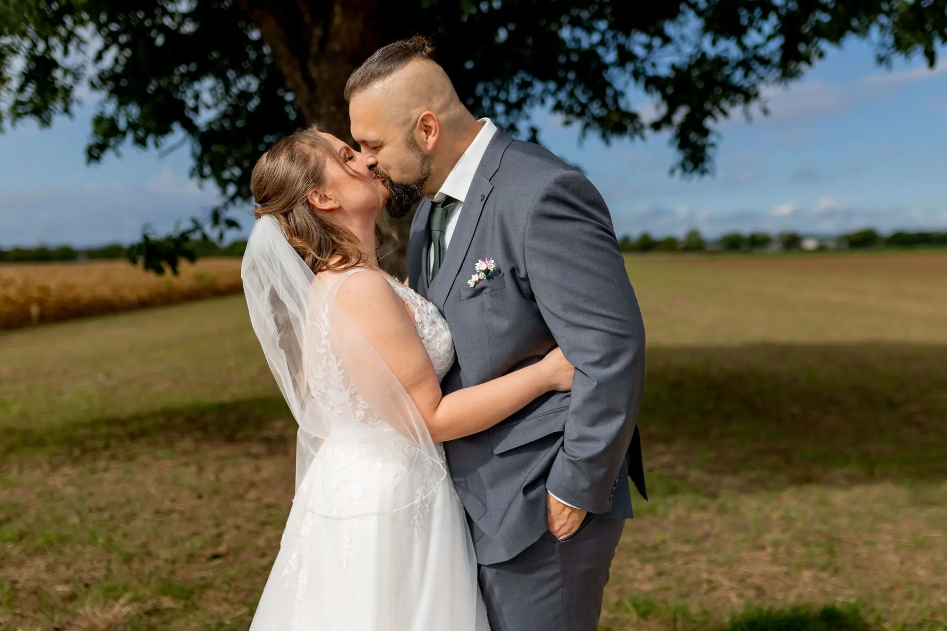 Brautpaar küsst sich unter einem Baum auf der Wiese