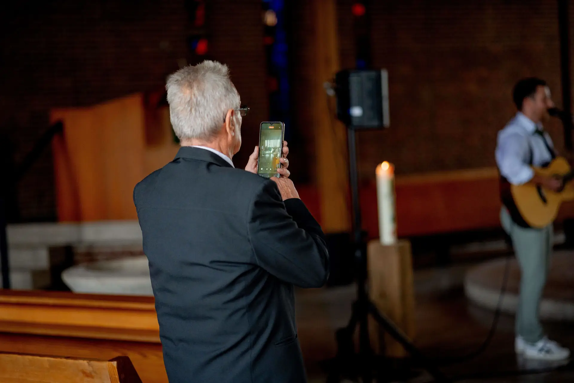 Gast filmt mit dem Handy während Gitarrist im Hintergrund spielt
