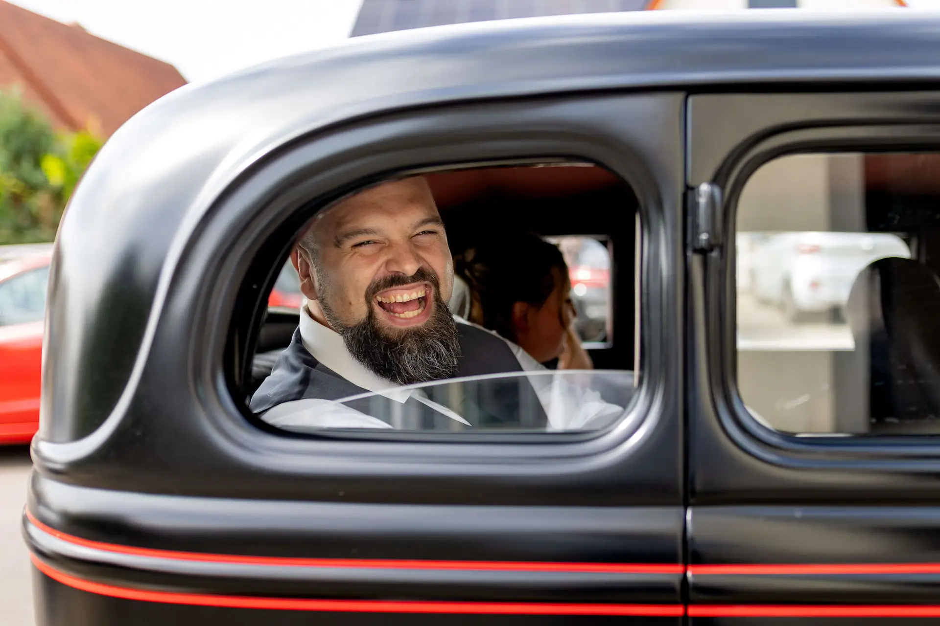 Bräutigam lacht aus dem Fenster des schwarzen Oldtimers