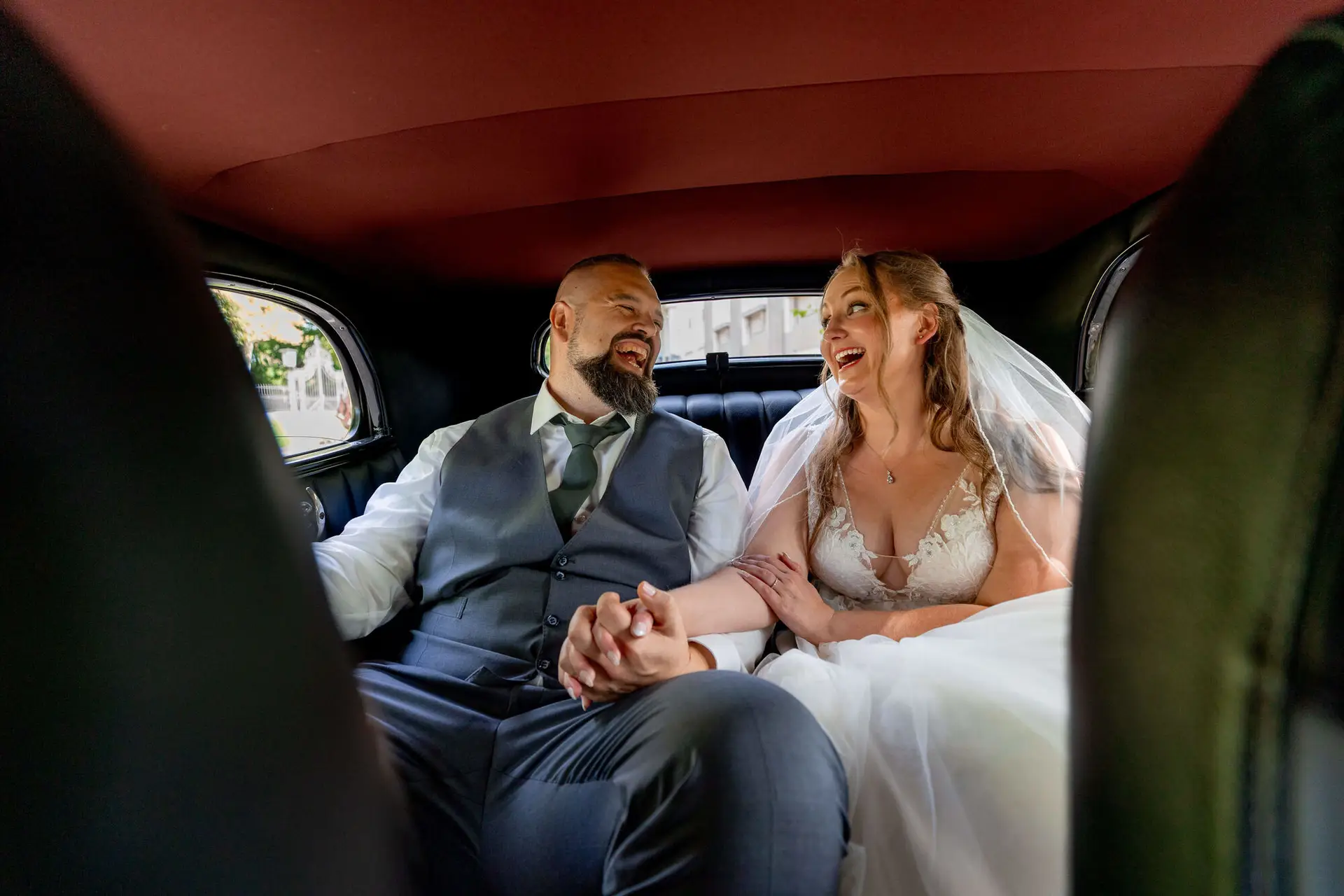 Brautpaar lacht zusammen auf der Rückbank des Oldtimers