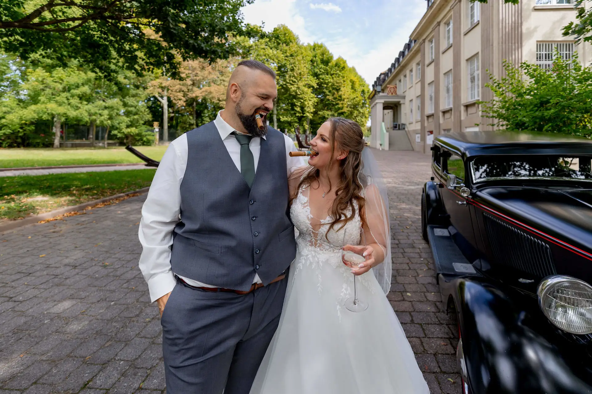Brautpaar geht lachend neben dem schwarzen Oldtimer