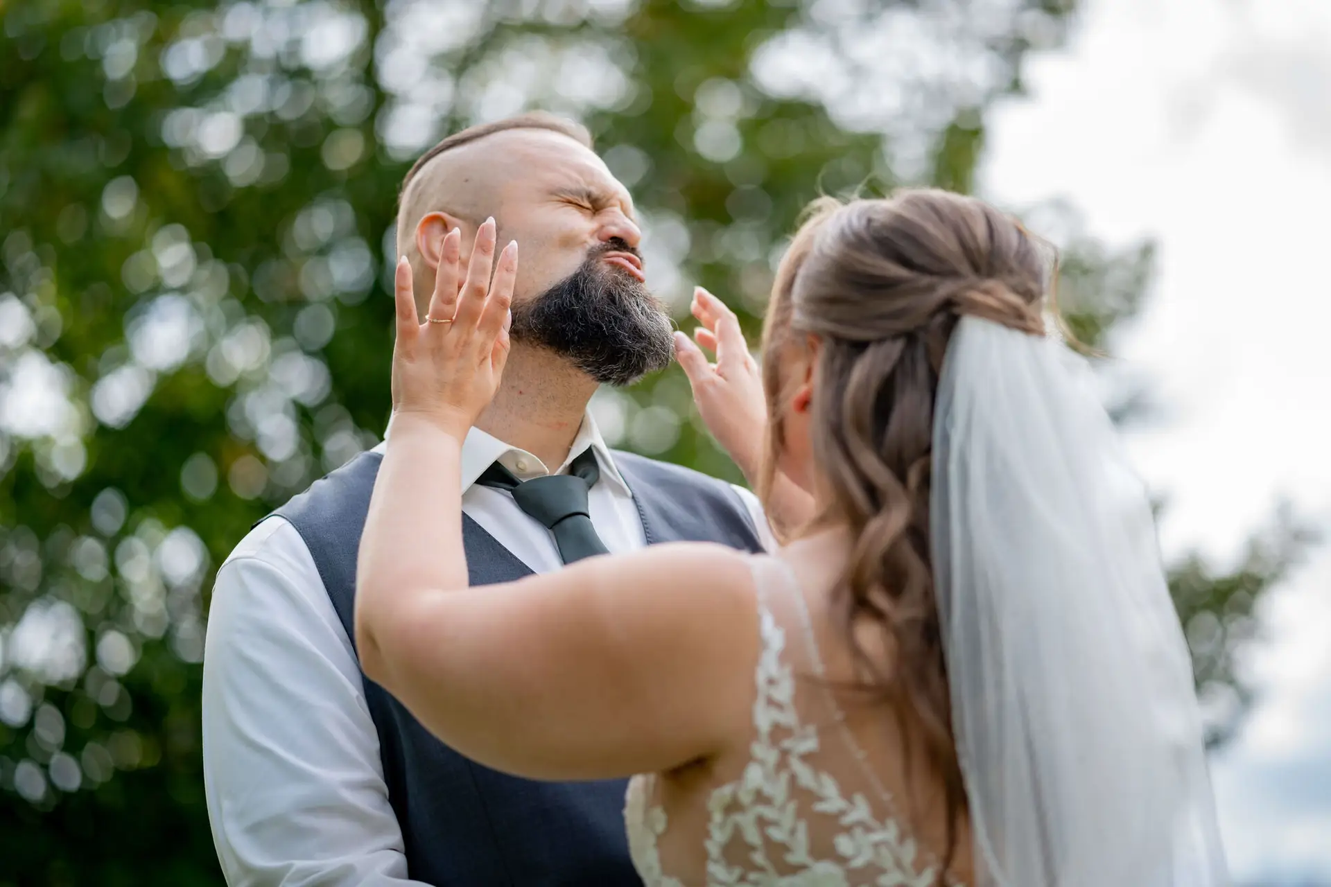 Braut drückt spielerisch die Wangen des Bräutigams zusammen