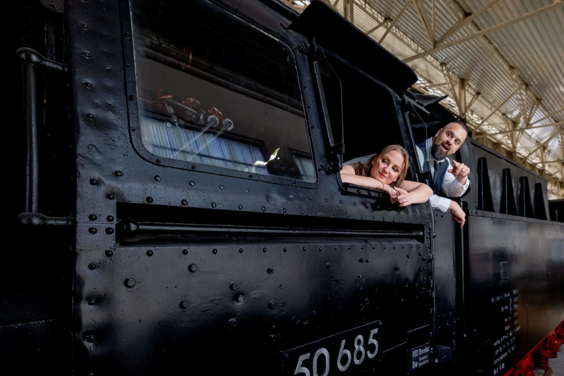 Brautpaar lehnt sich aus der Dampflok und lächelt in die Kamera