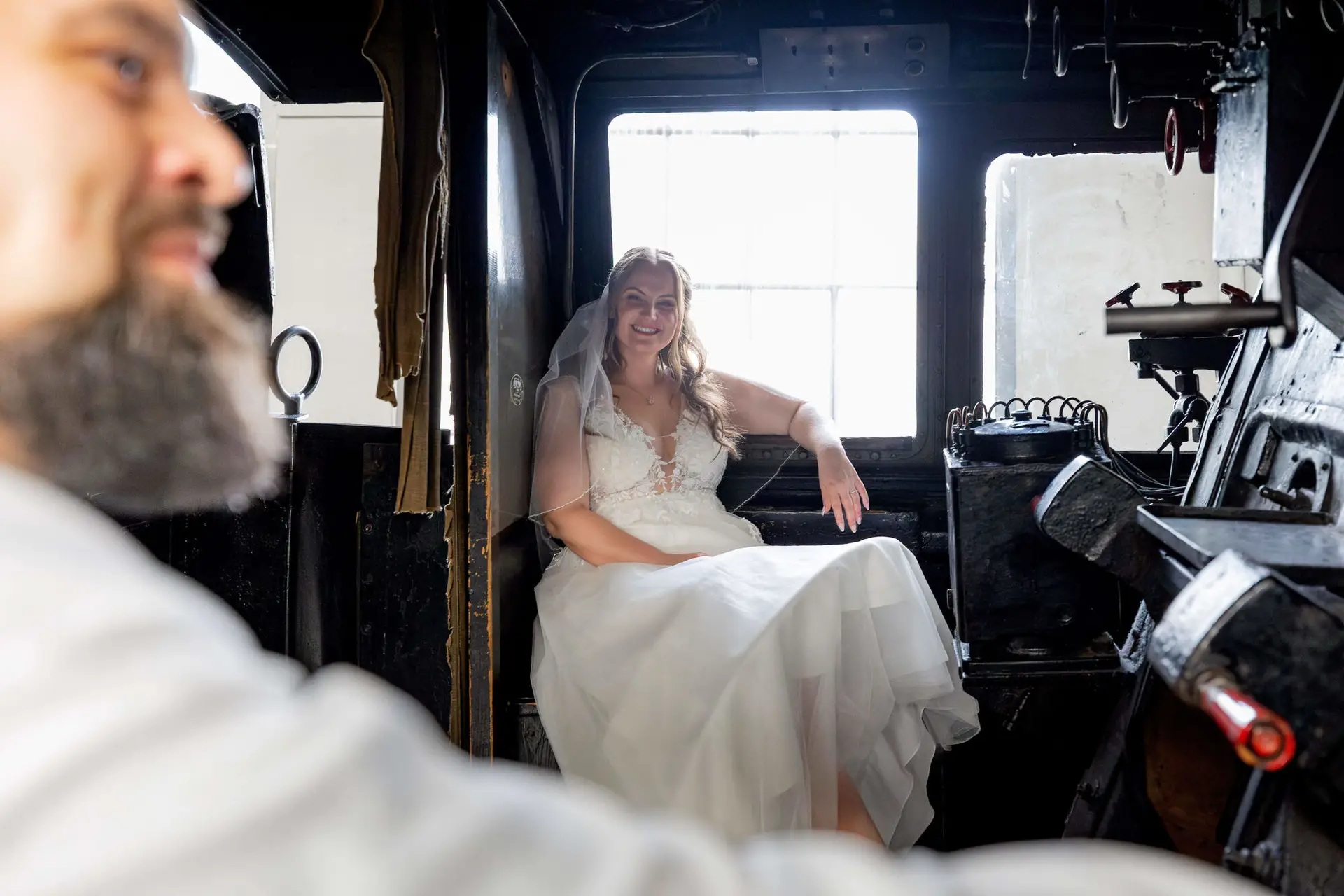 Braut sitzt lächelnd im Führerstand der Dampflok im Gegenlicht