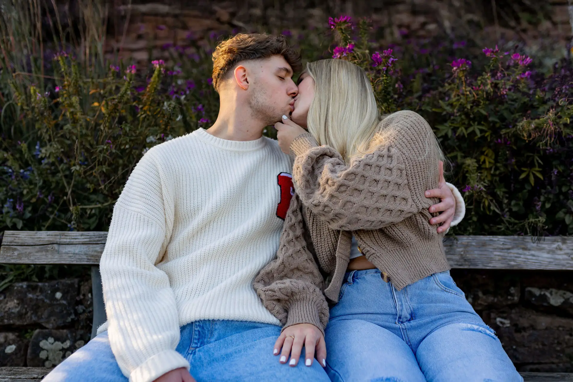 Sebi und Lena küssen sich auf einer Bank im Philosophengärtchen, lila Blumen im Hintergrund