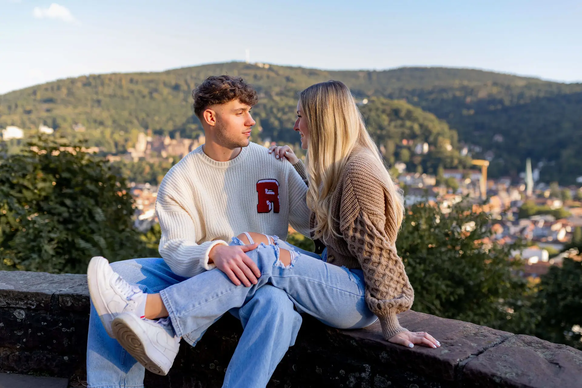 Sebi und Lena schauen sich verliebt an auf der Mauer im Schlossgarten mit Blick über Heidelberg