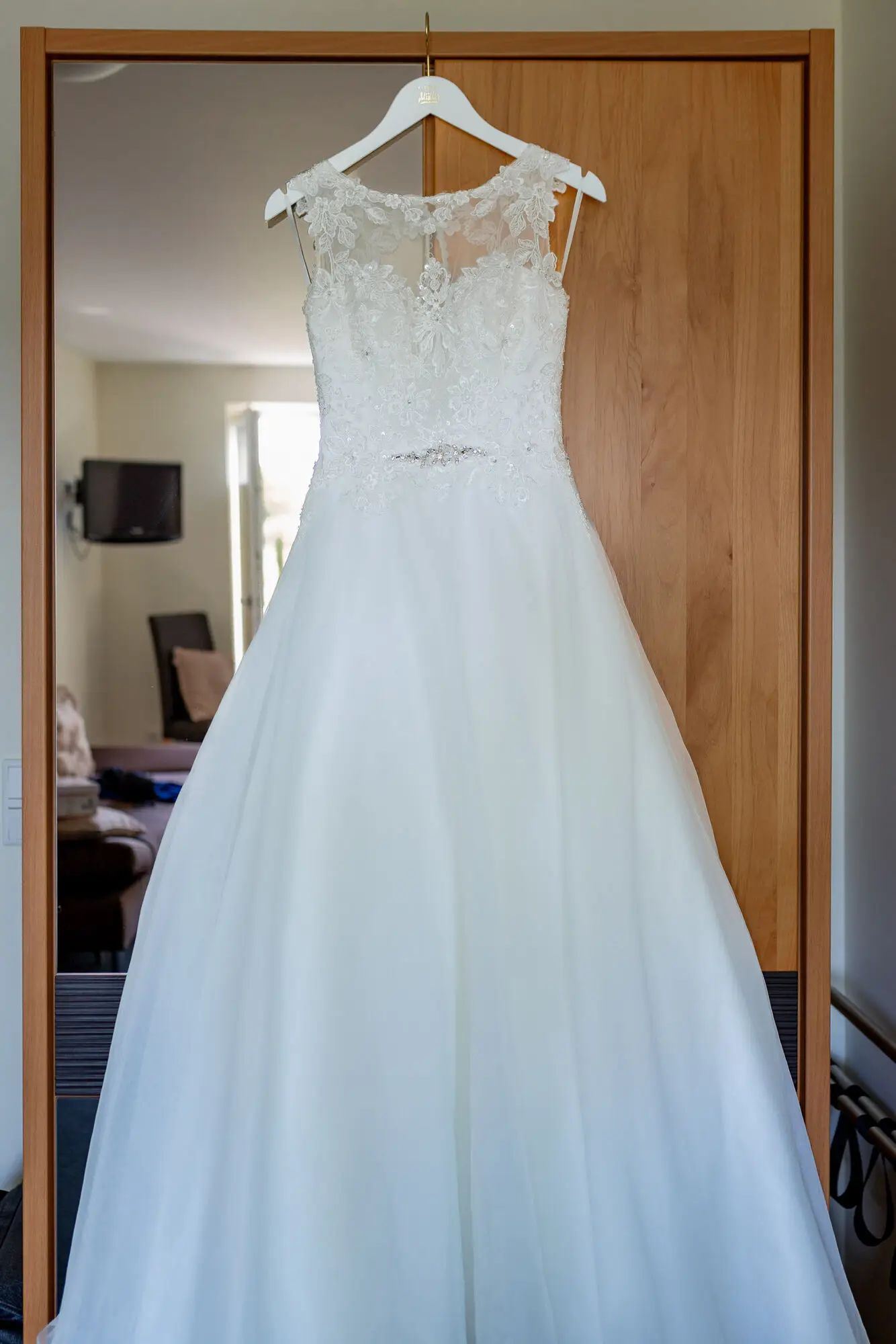 Weißes, glitzerndes Hochzeitskleid mit Volants und Spitze hängt an einem Schirm vor altem Holztor