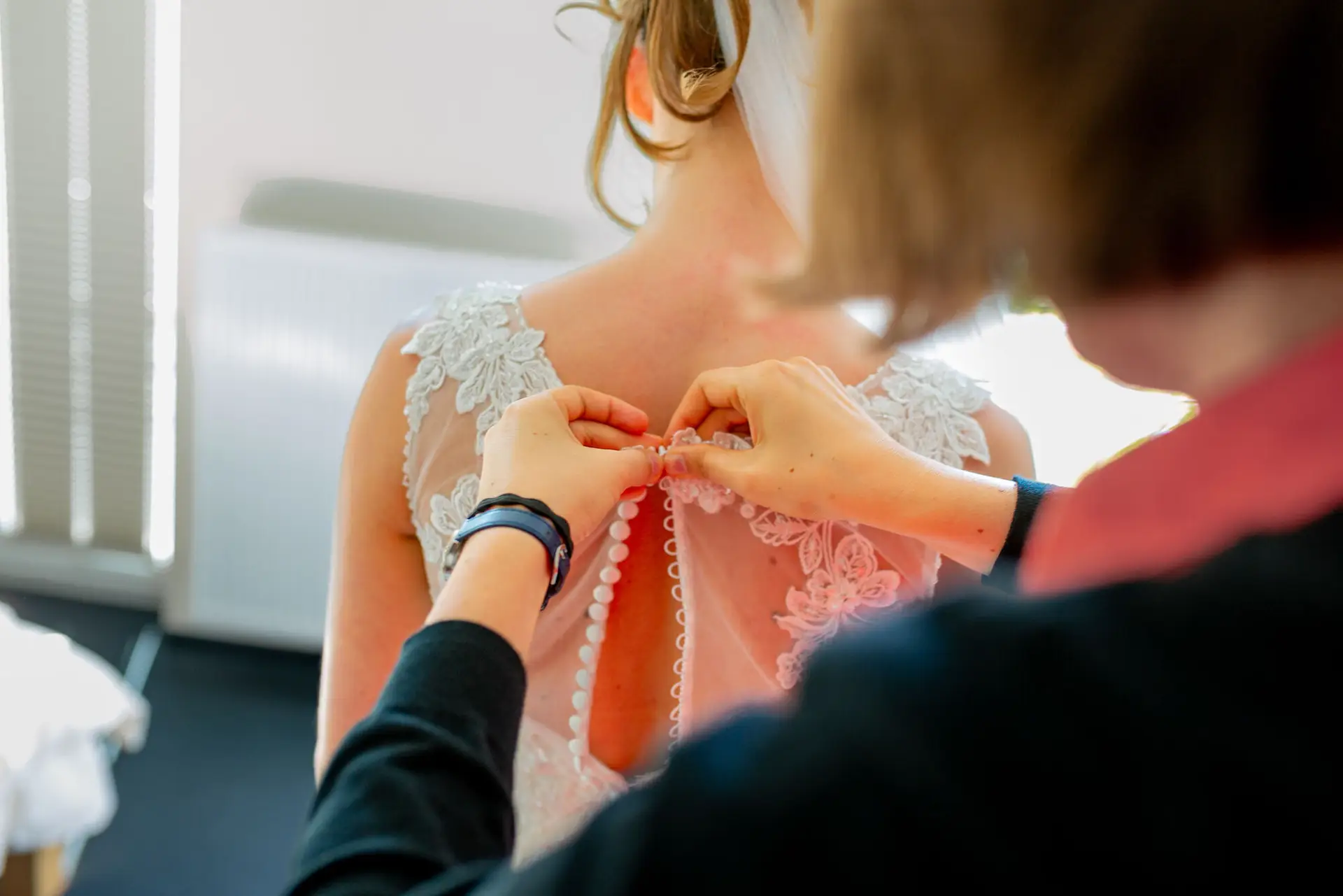 Hand befestigt zart weiße Perlen am Rücken des hochgesteckten, blumengeschmückten Brautkleides