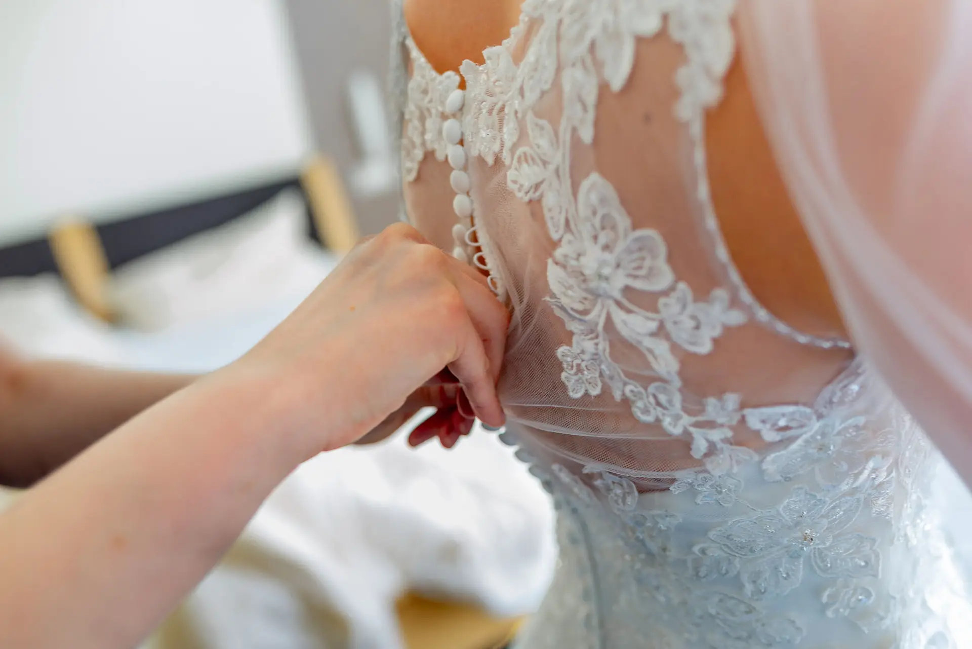 Hand justiert feines Spitze-Detail am Rücken des hochgeschlossenen weißen Brautkleides