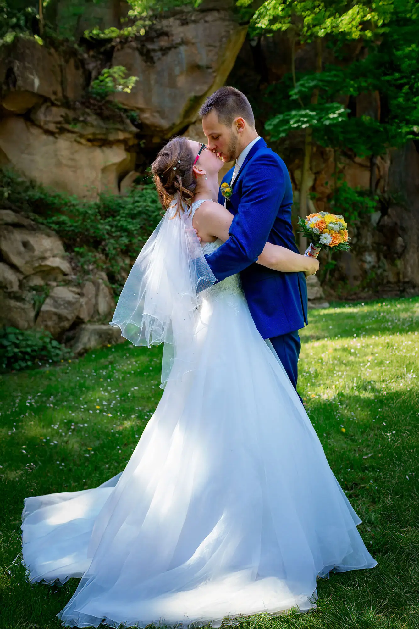 Bräutigam umarmt seine Braut zärtlich unter grünen Felsen beim Shooting in der freien Natur