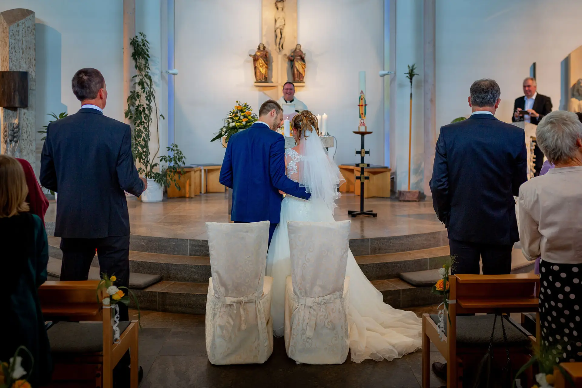 Brautpaar küsst sich beim ersten Kuss in der Kirche, Gäste im Kirchenschiff applaudieren gerührt