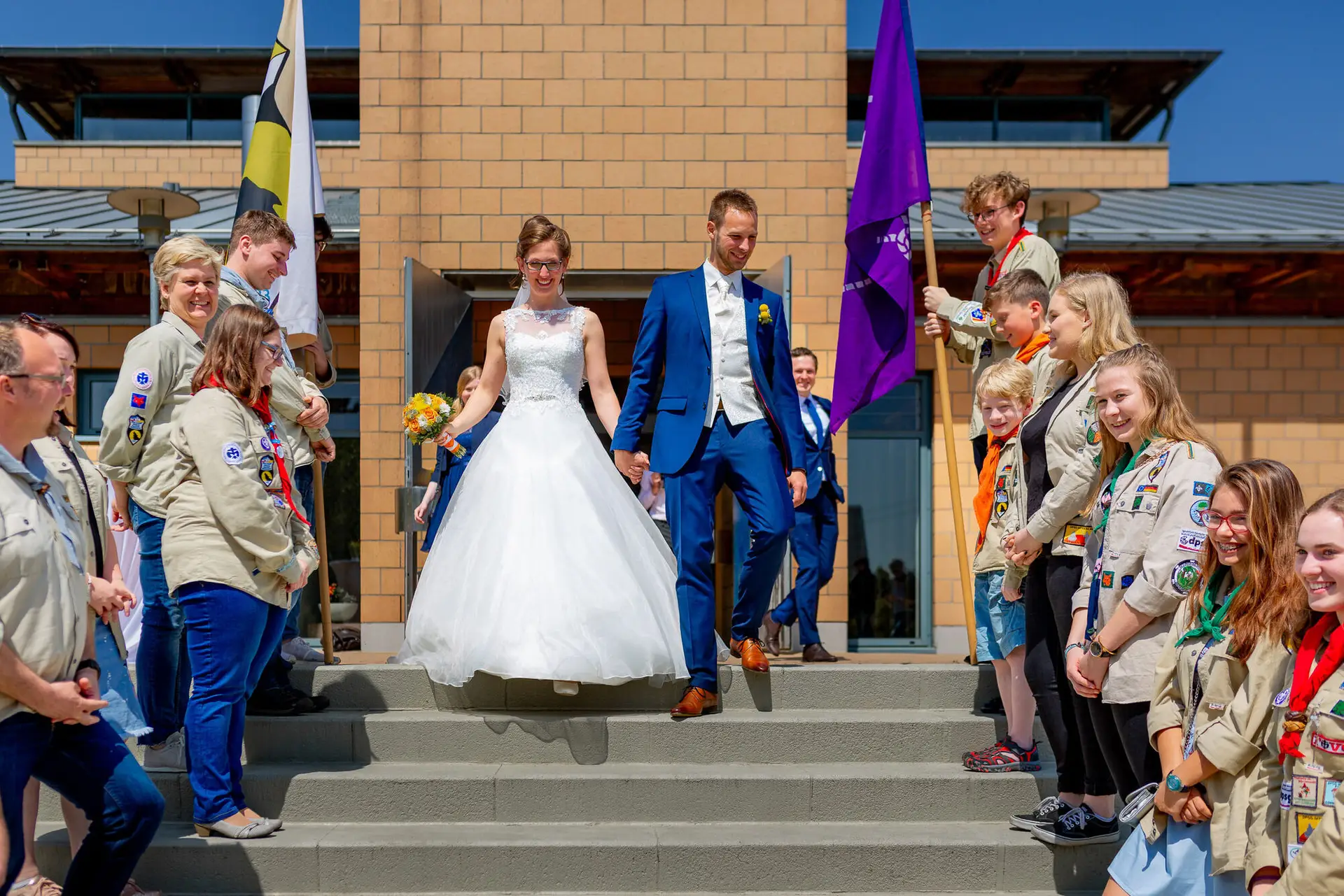 Bräutigam führt das Brautpaar gemeinsam mit Kindern in Pfadfinder-Shirts auf eine Treppe bei der Zeremonie