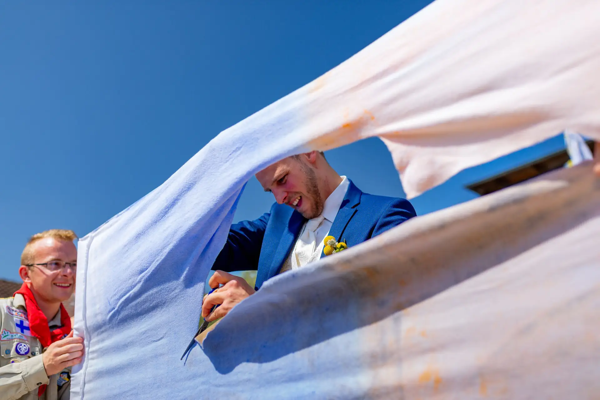 Brautpaar steht unter weißem Tuch im Freien, Trauzeugen und Gäste rahmen das Paar bei strahlendem Sonnenschein ein