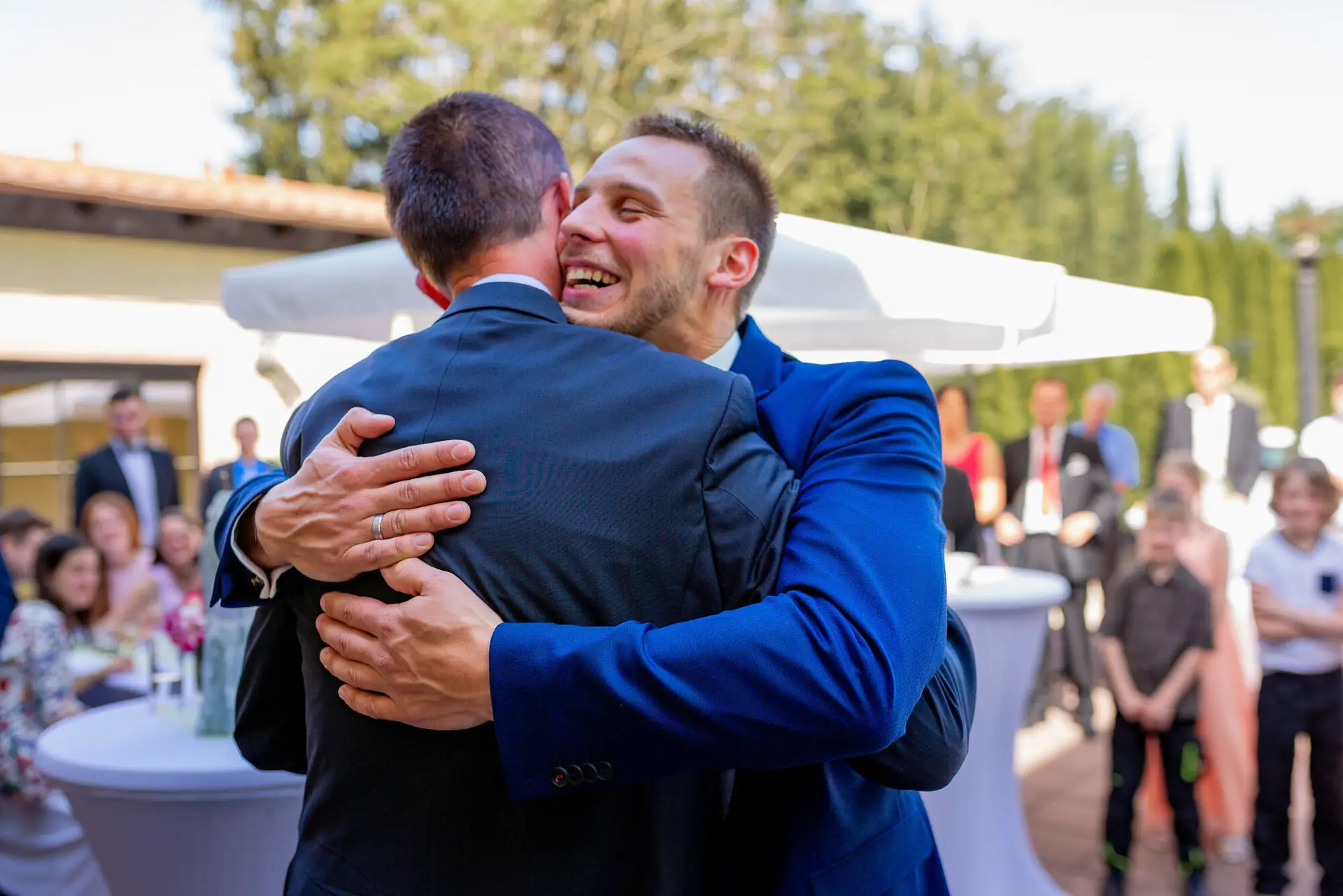 Zwei junge Männer umarmen sich überglücklich beim Wiedersehen auf dem Hochzeitsgelände
