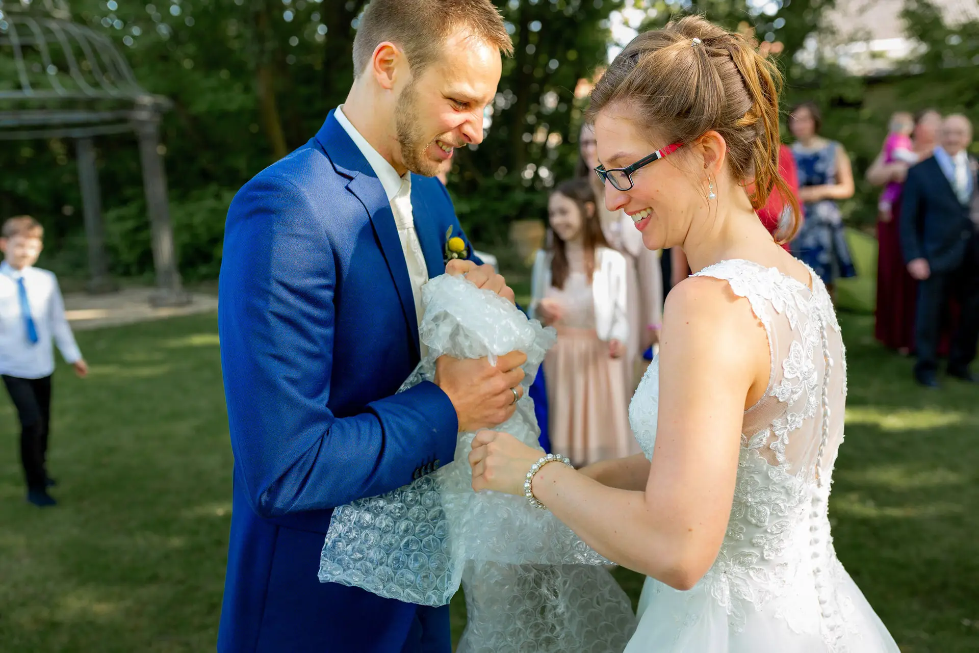 Bräutigam überreicht seiner lachenden Braut ein Seifenblasen-Set auf der grünen Wiese beim Sektempfang