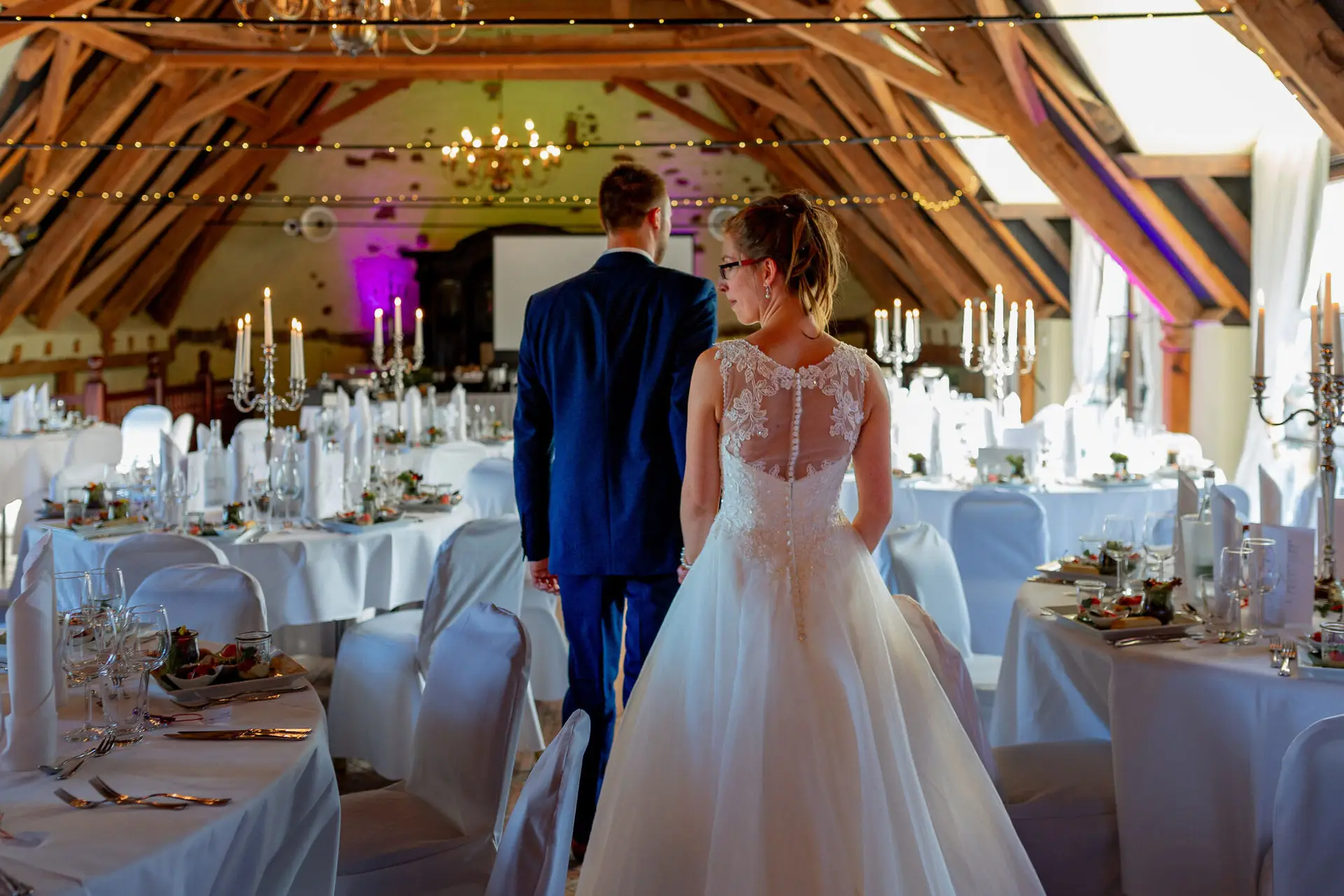 Brautpaar schreitet gemeinsam durch prachtvollen Saal mit Kerzen und Festbeleuchtung