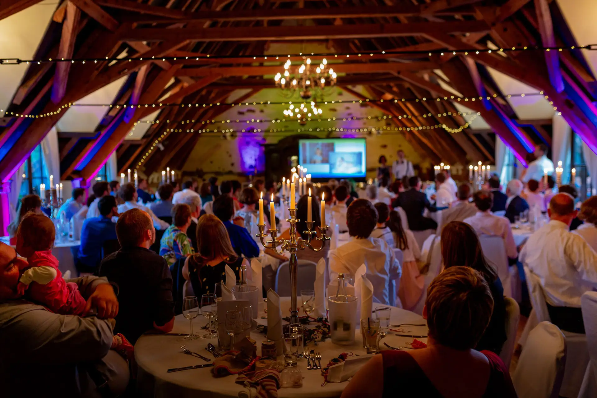 Hochzeitsdinner in strohgedecktem Saal mit beleuchteten Tischen, Kerzen und vielen fröhlichen Gästen