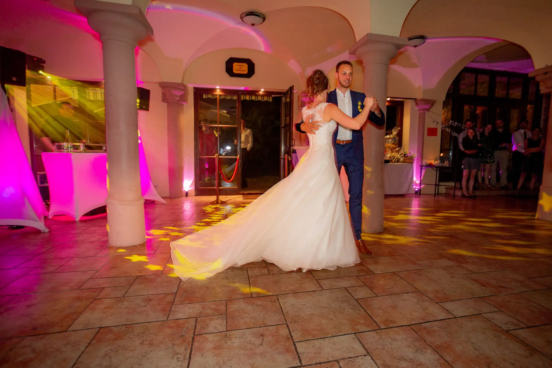 Brautpaar tanzt gemeinsam im rosa und gelben Scheinwerferlicht beim ersten Hochzeitstanz