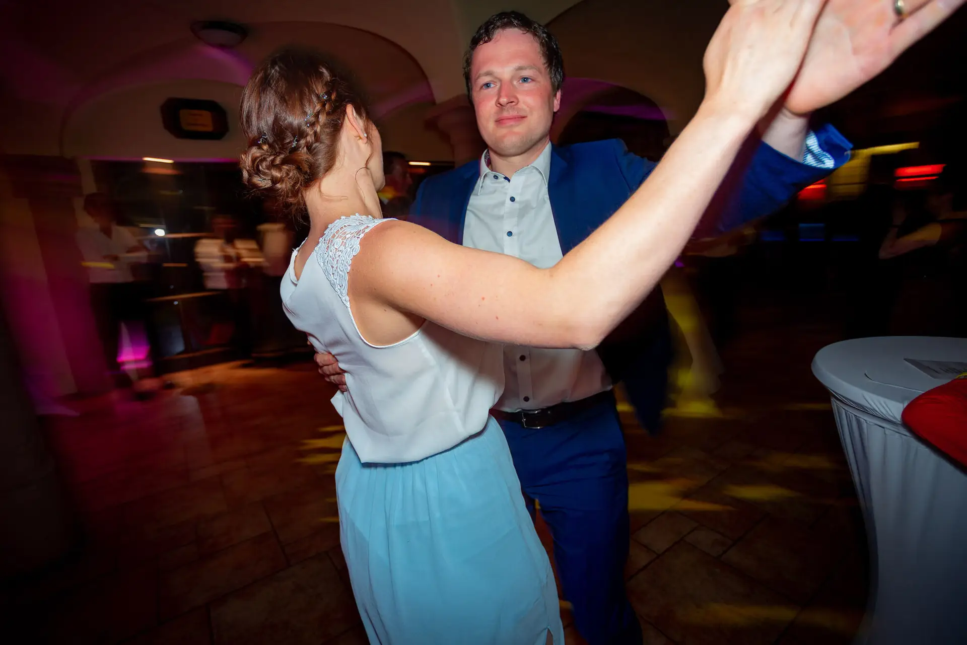 Brautpaar tanzt innig im Lichtschein der Hochzeitsparty, Mann hält die Hand seiner Partnerin