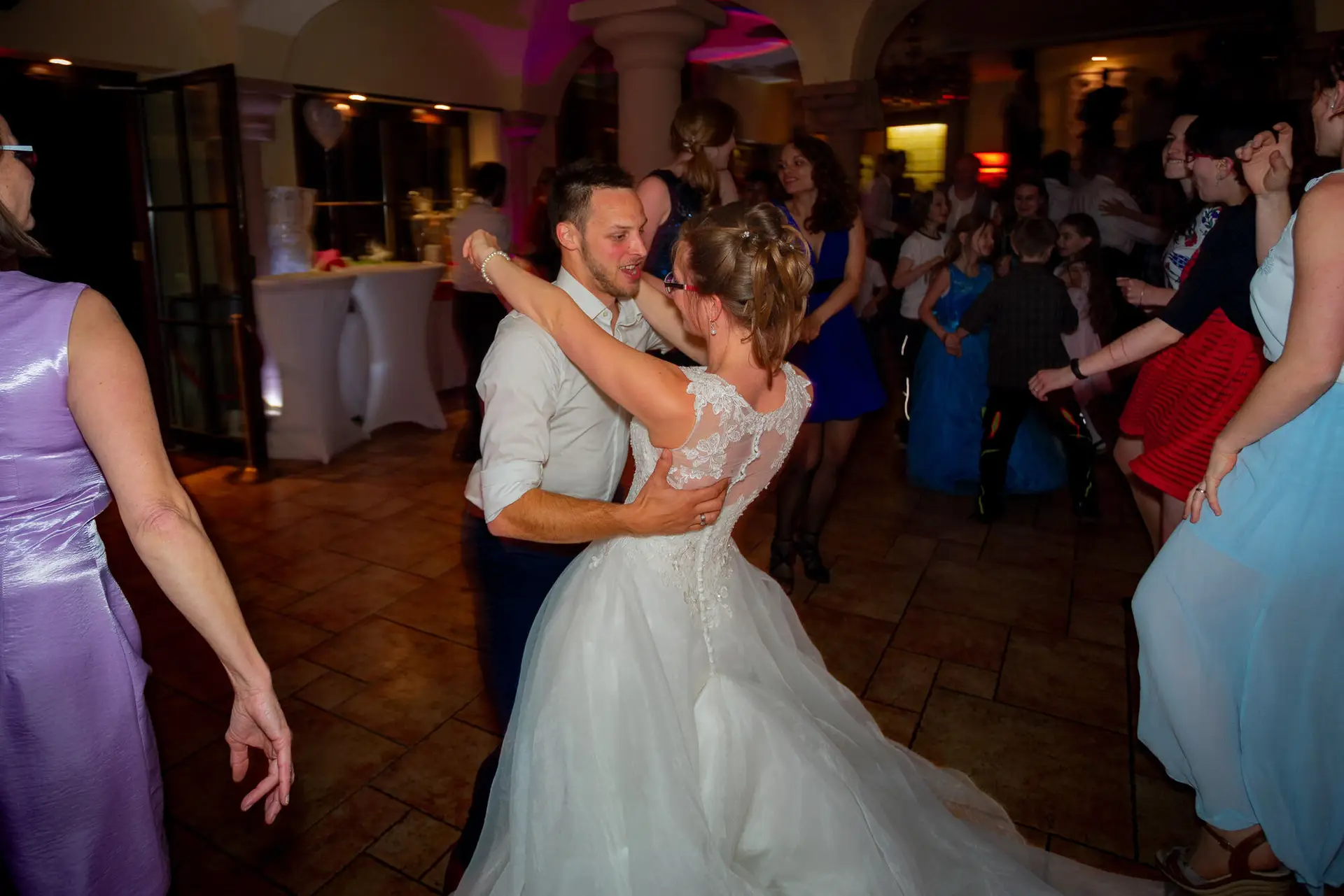Brautpaar tanzt ausgelassen mit Hochzeitsgästen auf dem belebten Hochzeitsballsaal