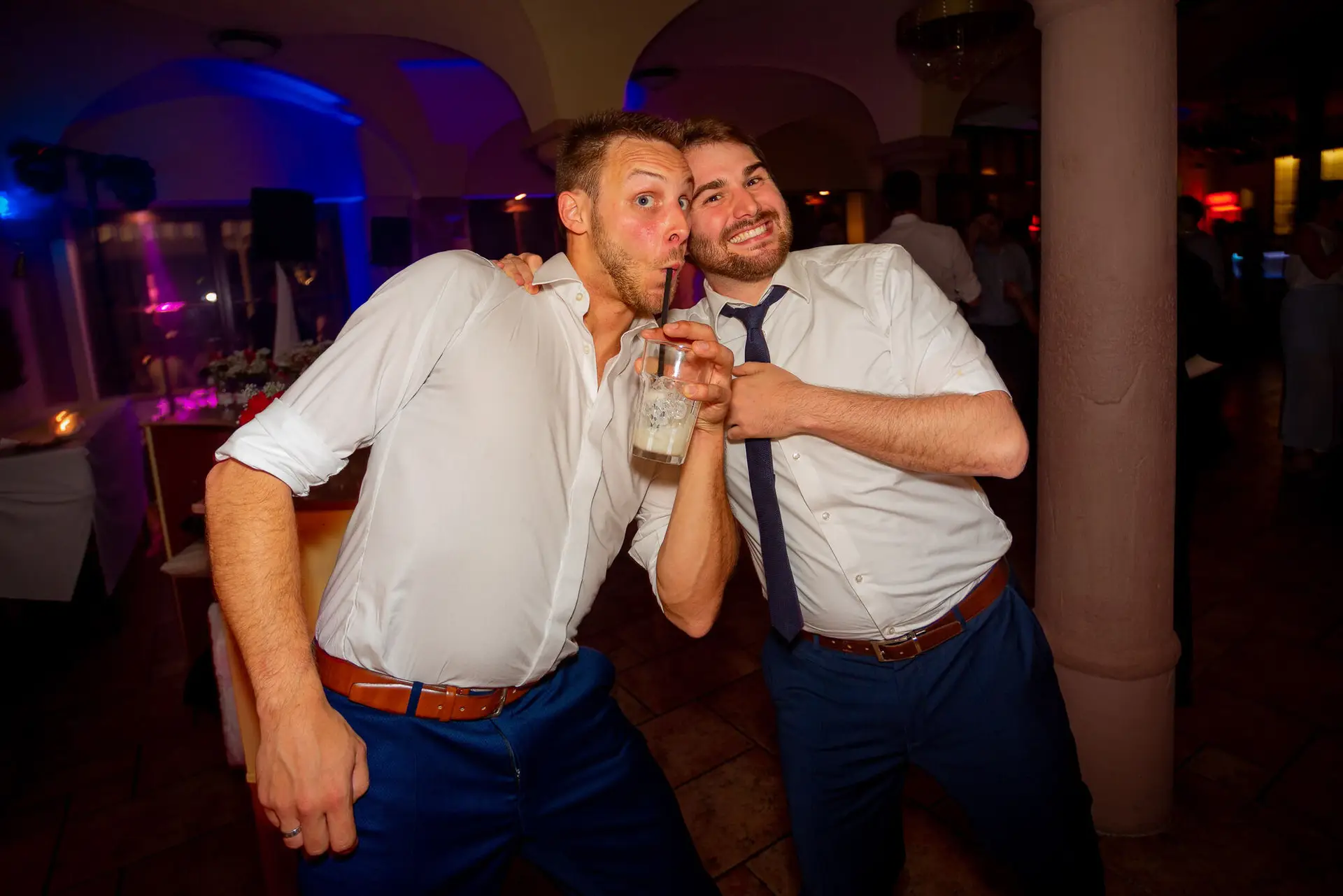 Zwei Freunde tanzen ausgelassen auf der Tanzfläche, einer hält ein Getränk in der Hand