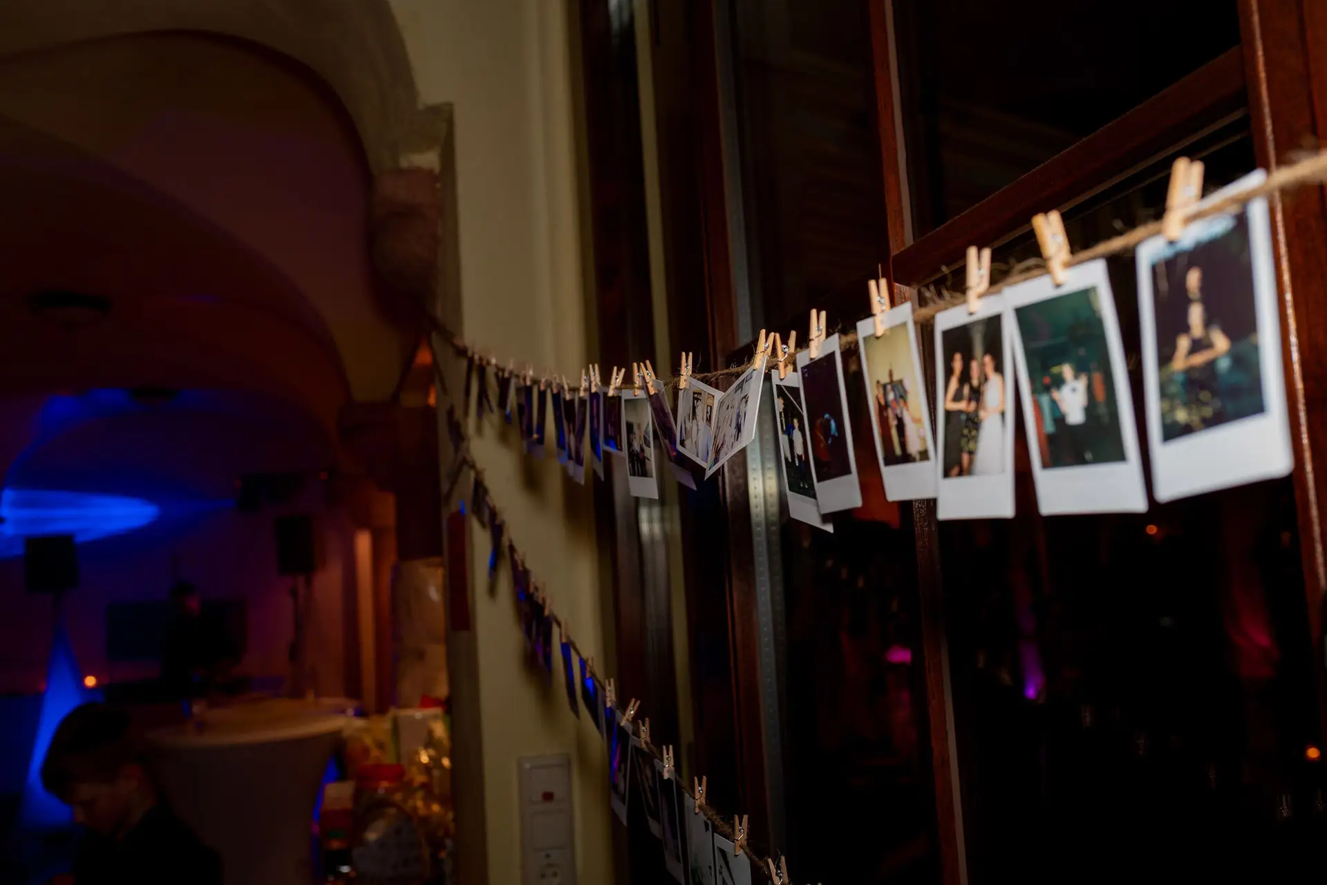 Girlande mit Polaroid-Hochzeitsfotos hängt dekorativ an dunklem Holzrahmen im festlich beleuchteten Saal