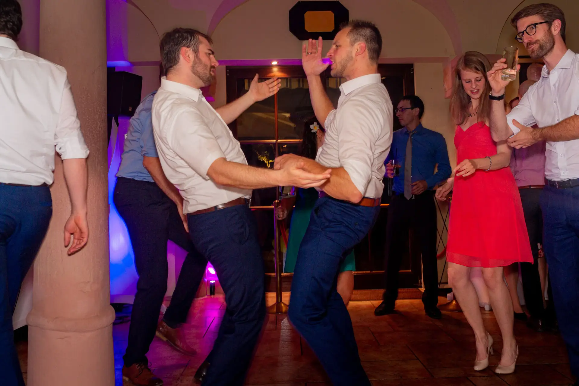Zwei Männer tanzen begeistert auf der Hochzeitsfeier, eine Frau beobachtet sie lächelnd