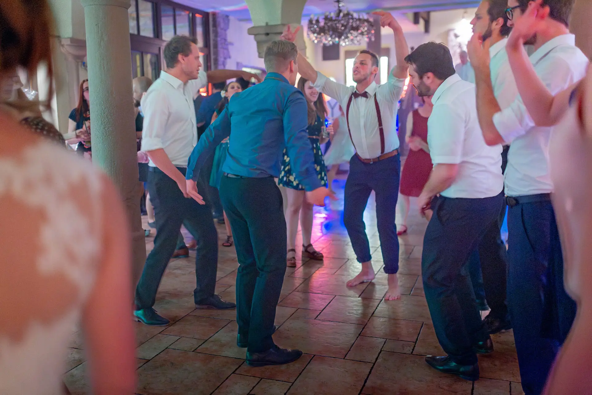 Paare tanzen ausgelassen auf der festlichen Hochzeitstanzfläche mit Kronleuchter im Hintergrund