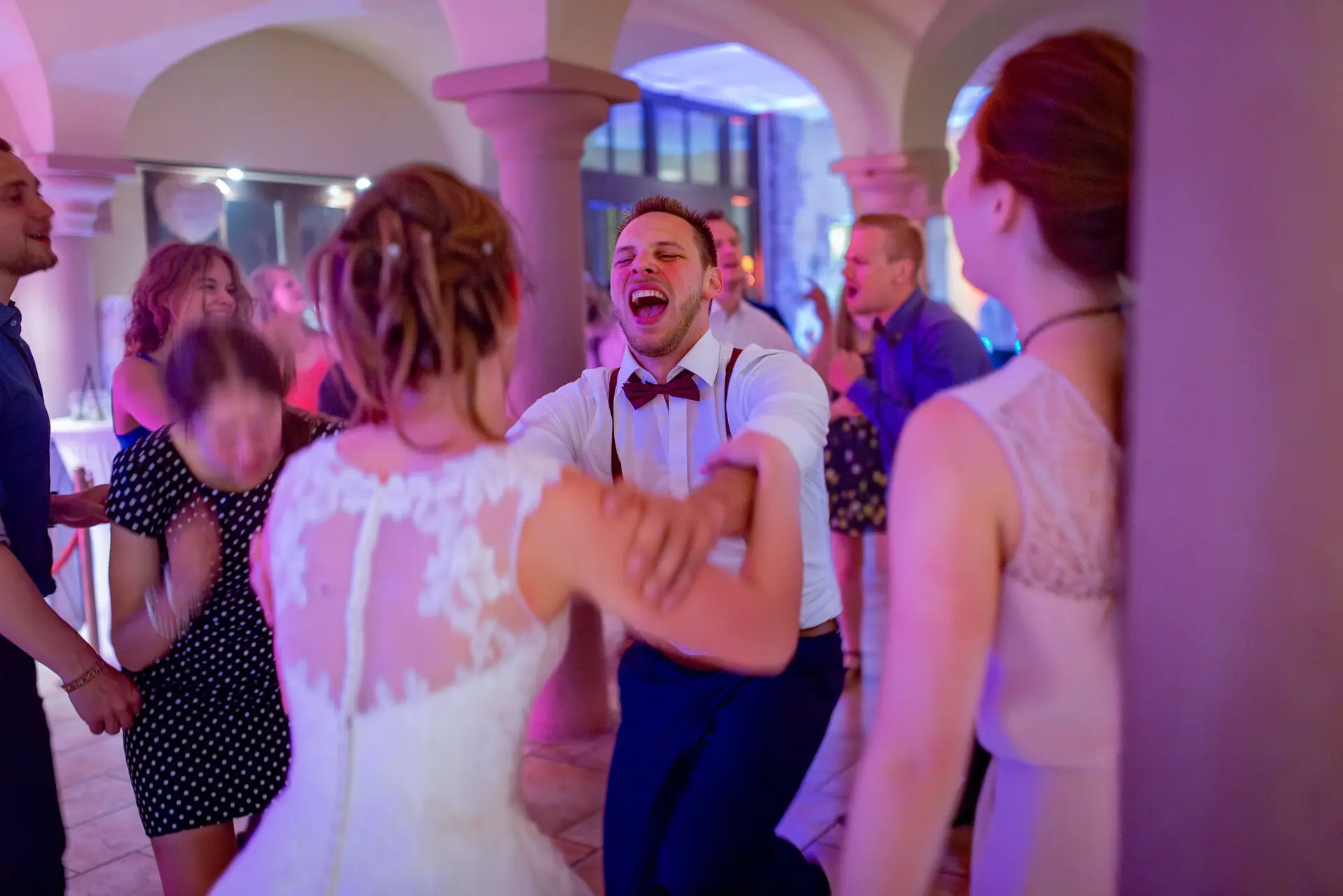 Jubelnder Gast in Weste tanzt mitreißend mit der Braut im Disco-Licht der Hochzeitsparty