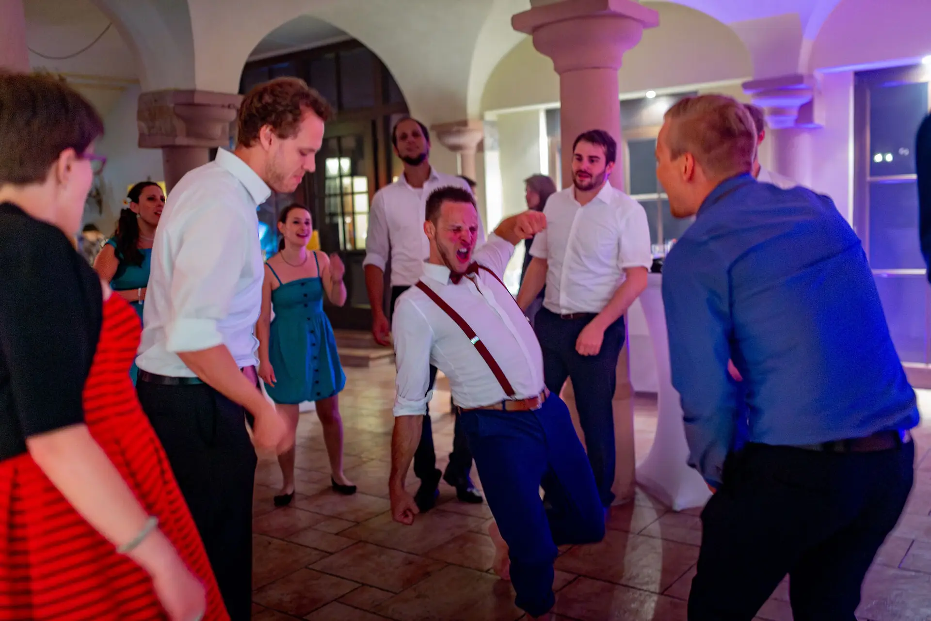 Gast tanzt ausgelassen mit anderen Feiernden in prächtigem Hochzeitssaal unter Kronleuchter