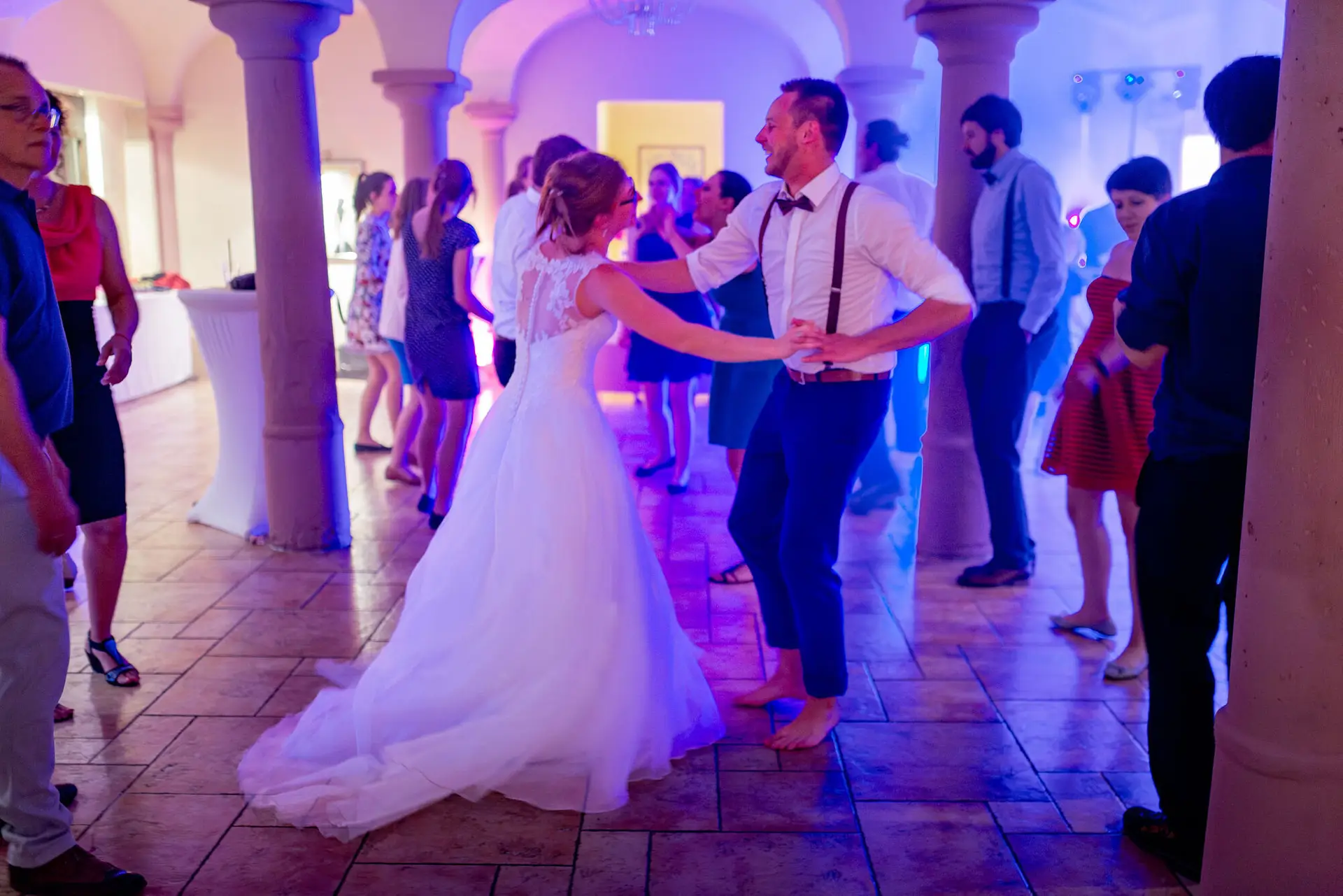 Brautpaar tanzt ausgelassen im blauen Scheinwerferlicht in Saal mit Säulen bei der Hochzeitsparty