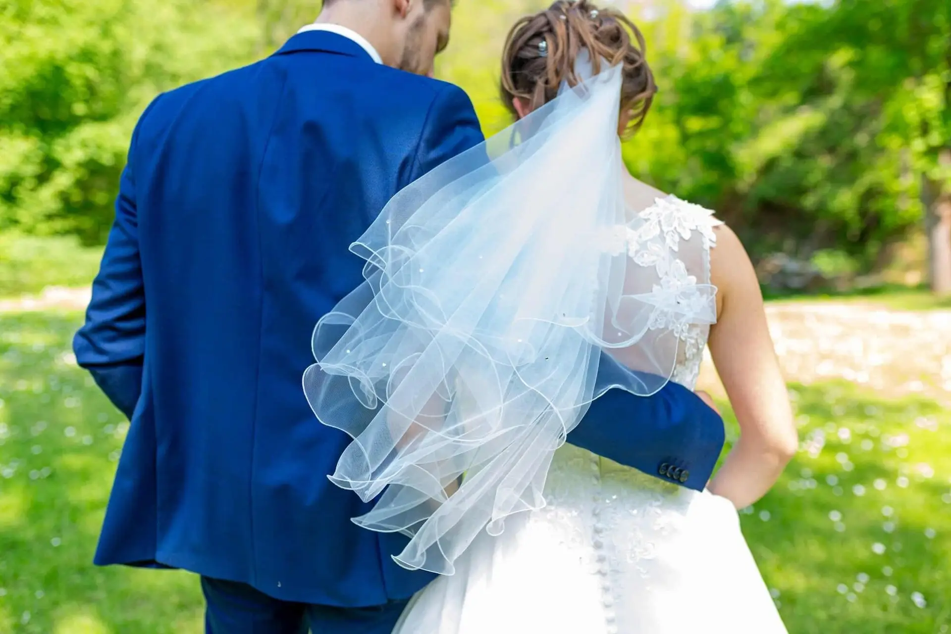 Brautpaar im Grünen, Braut mit Schleier und Bräutigam im blauen Jackett schauen sich an