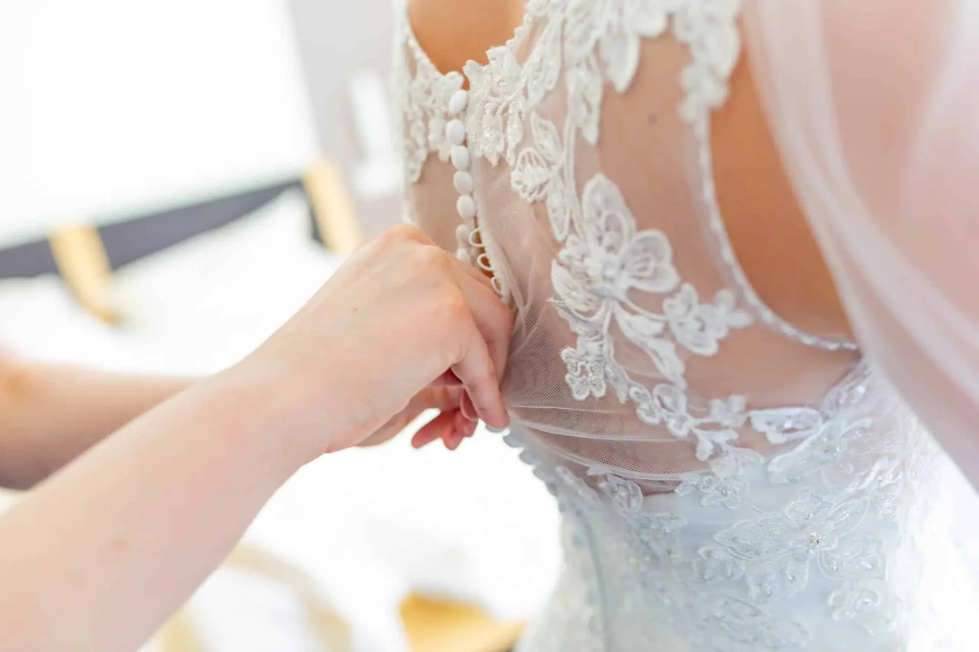 Nahaufnahme der Hand, die feines Spitzendetail am Rücken der Braut im hochgeschlossenen weißen Hochzeitskleid formt