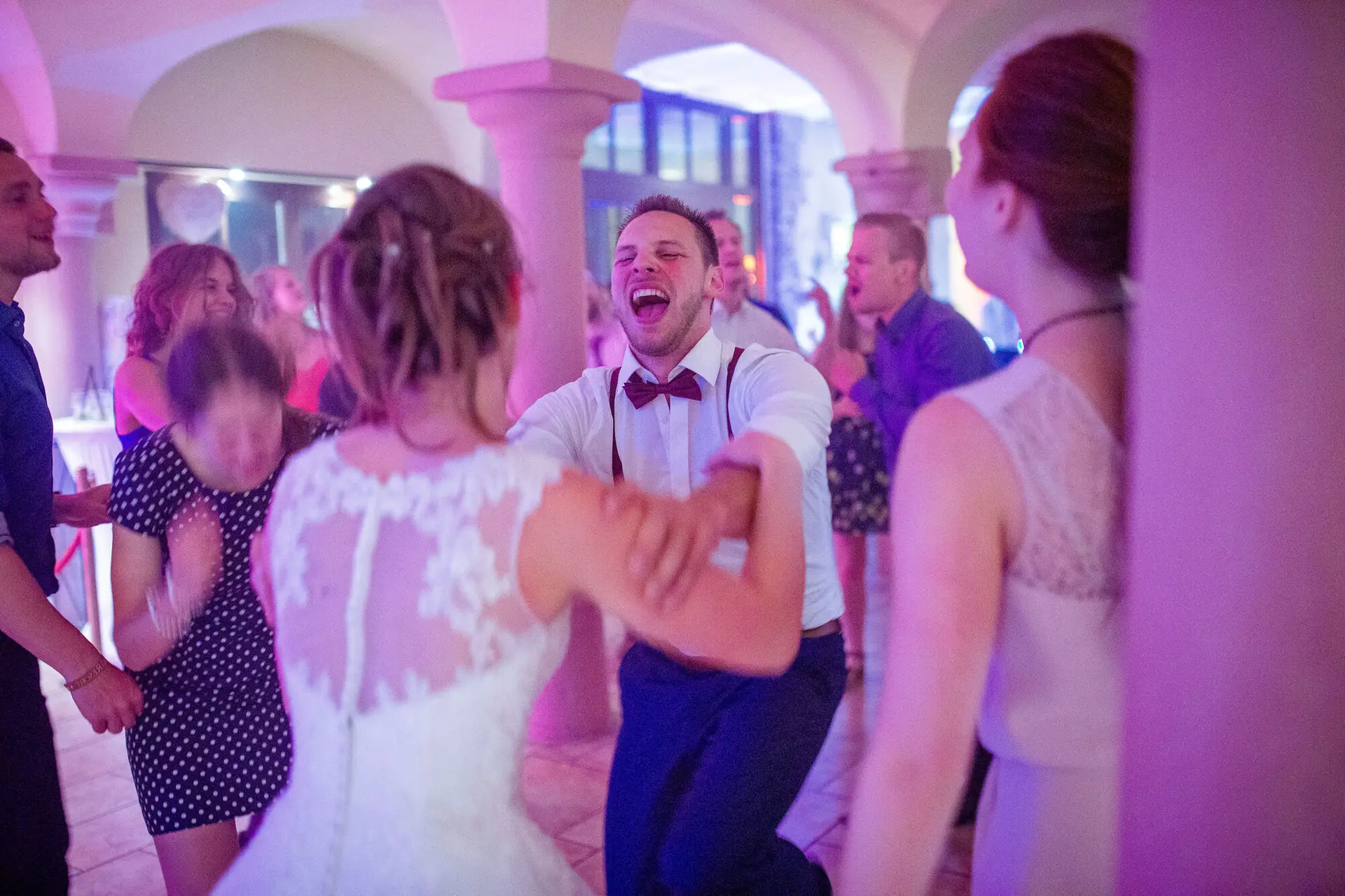 Jubelnder Bräutigam tanzt leidenschaftlich mit seiner Braut in rosa beleuchtetem Festsaal