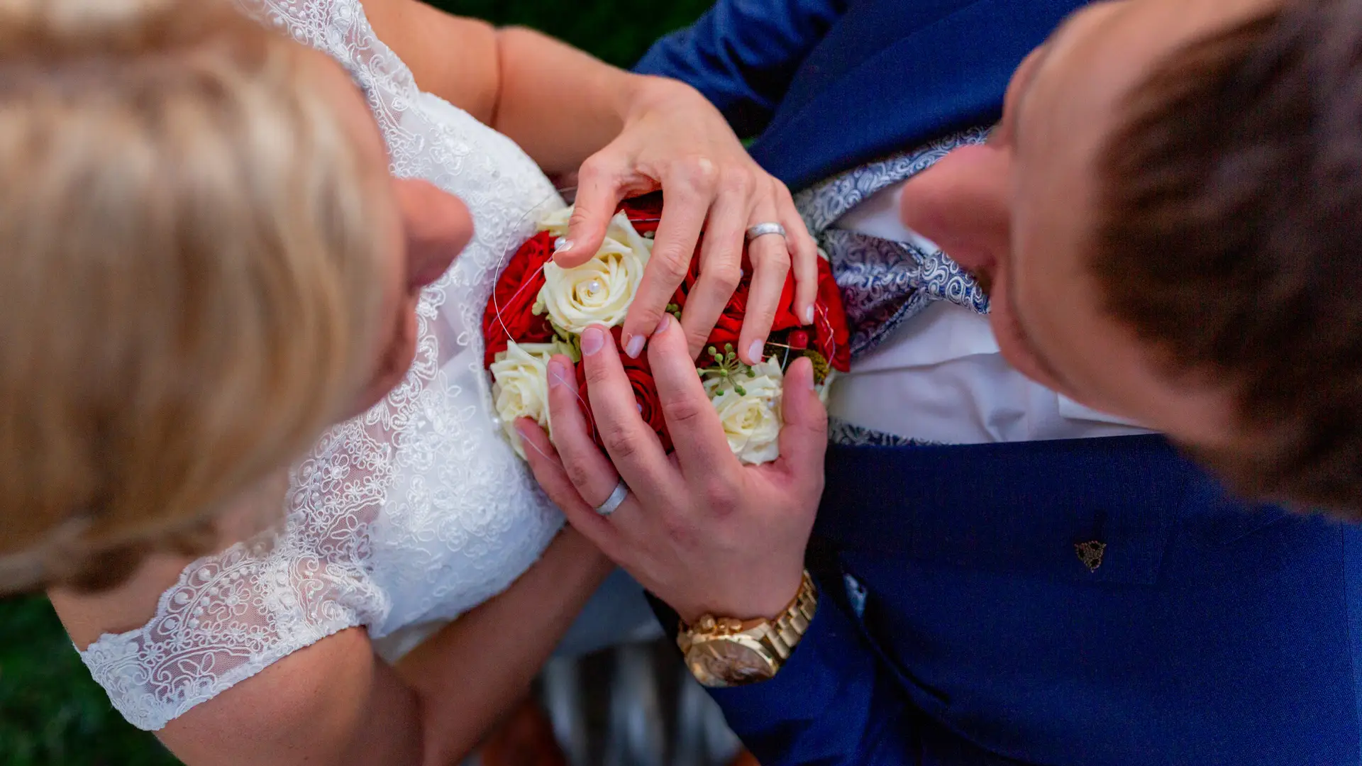 Hände des Brautpaares mit Eheringen auf dem rot-weißen Brautstrauß, Detailaufnahme von oben