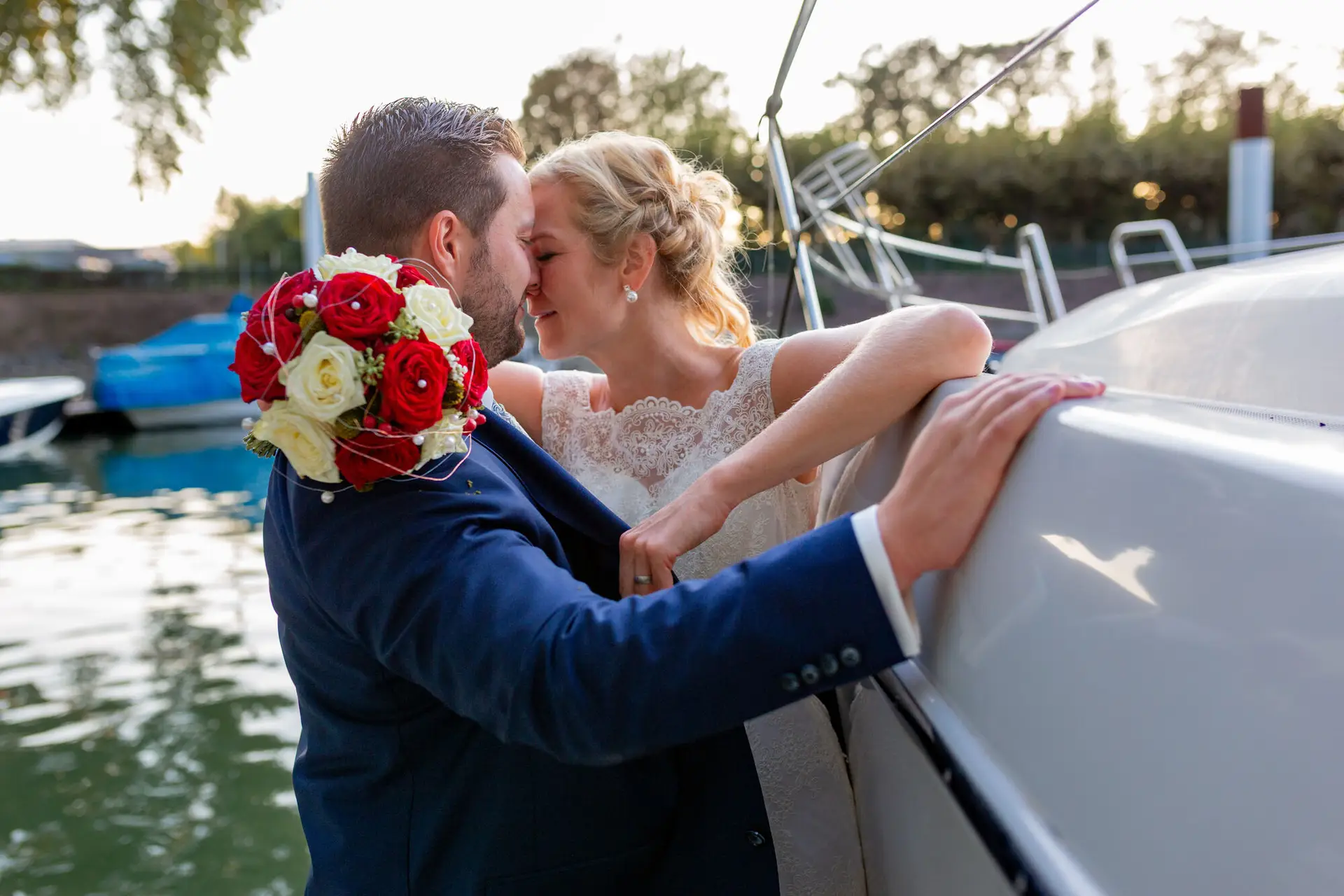 Anna Gregor Brautpaarshooting Worms Yachthafen Kuss Rote Blumen.8E E36Qf Brautpaar küsst sich an einem Boot im Yachthafen Worms, rot-weißer Brautstrauß im Vordergrund