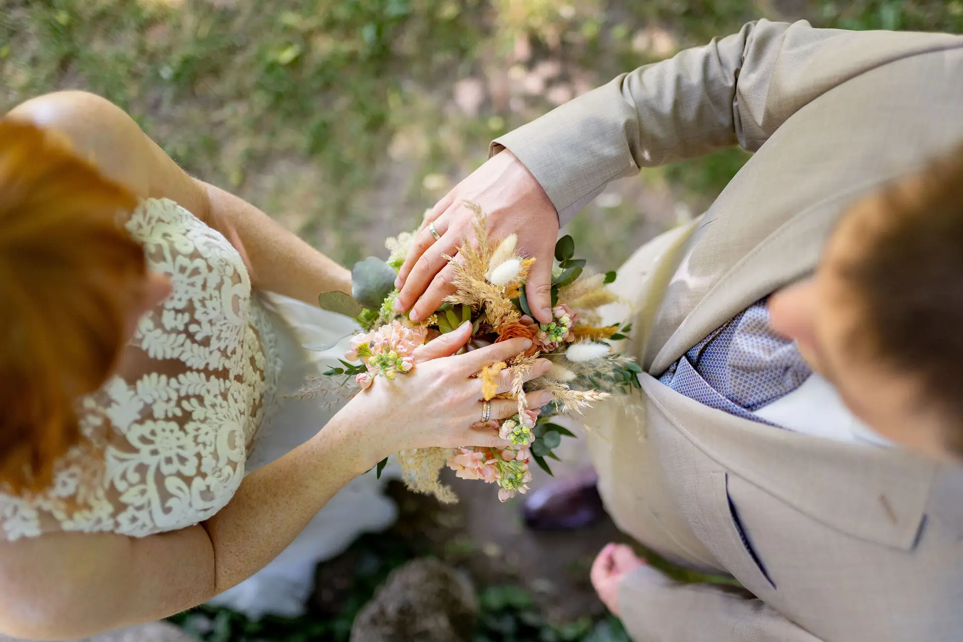 Hände des Brautpaares mit Eheringen auf dem Brautstrauß, Detailaufnahme von oben im Schlossgarten Herrnsheim