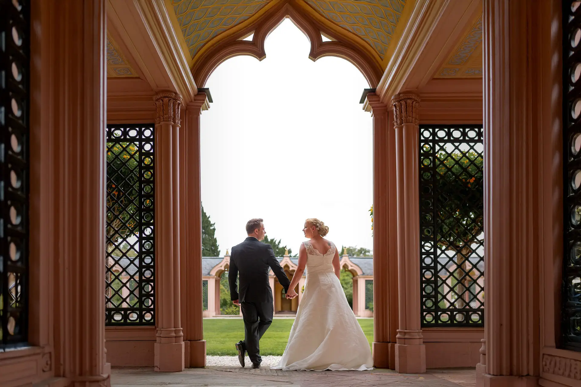 Brautpaar spaziert Hand in Hand durch das reich verzierte Portalbogentor im Schlossgarten Schwetzingen