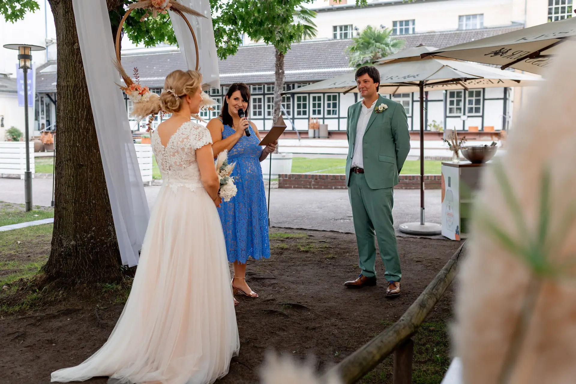 Traurednerin in blauem Kleid spricht bei der freien Trauung, Brautpaar steht sich gegenüber