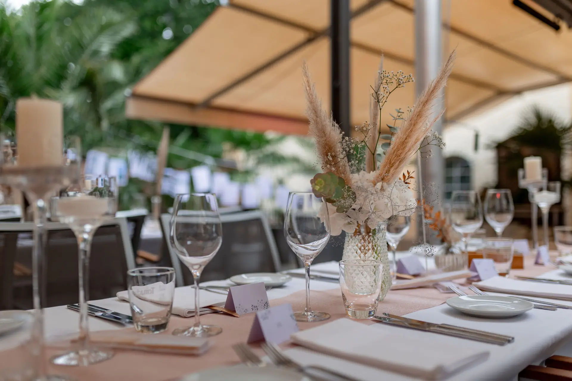 Tischdekoration mit getrockneten Gräsern und Grünpflanzen in Glasvasen auf dem festlichen Hochzeitstisch im Freien