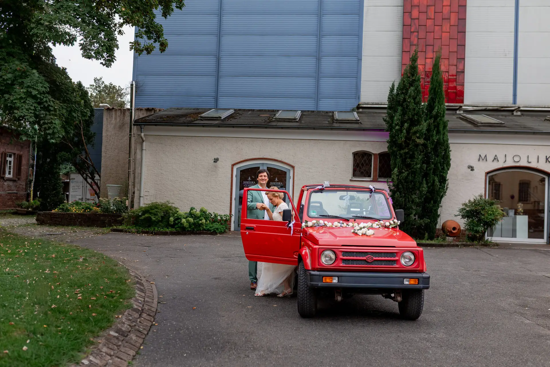 Rotes Fahrzeug mit Braut vor dem modernen Eingangsbereich der Hochzeitslocation in Karlsruhe