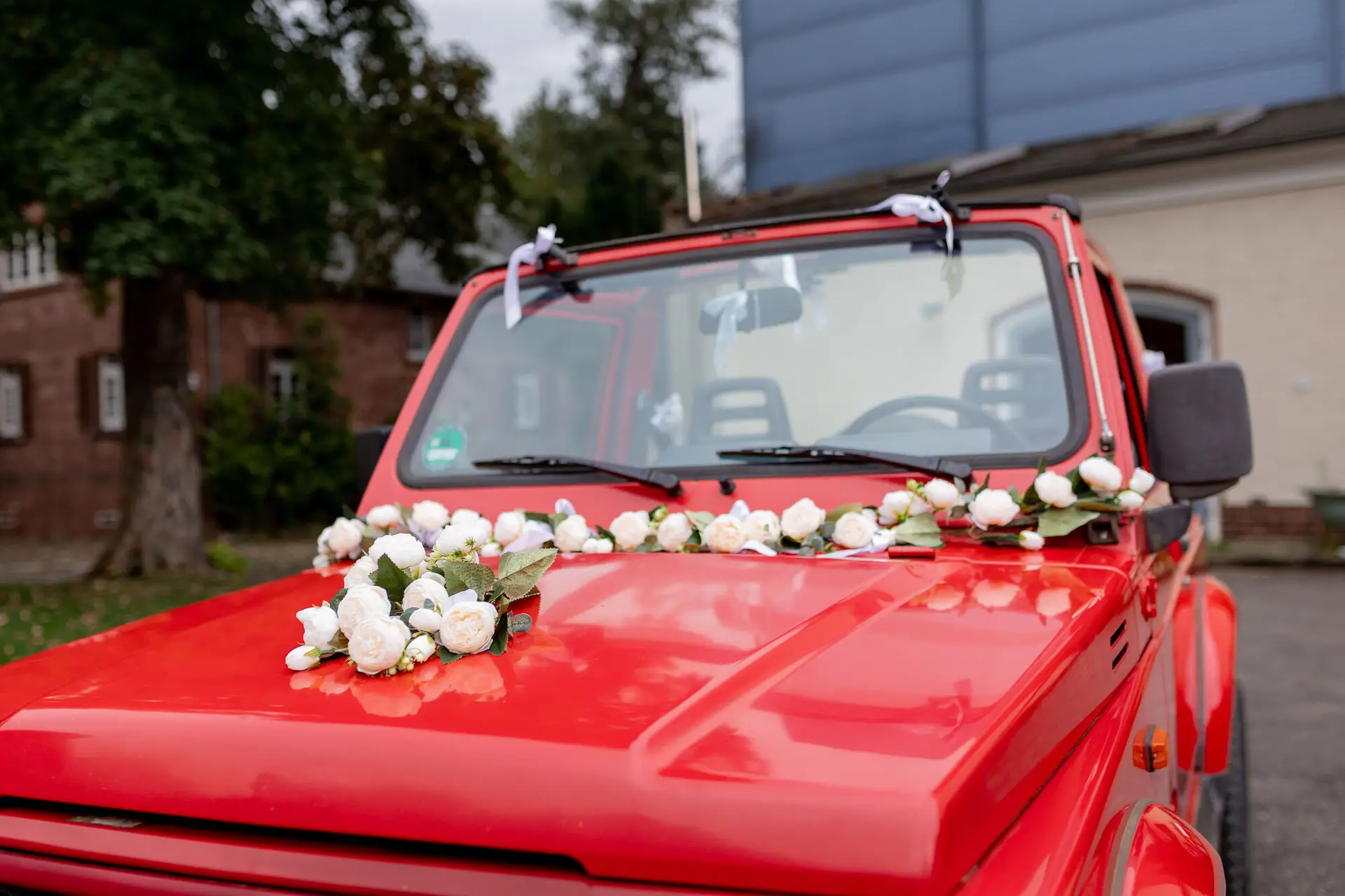 Motorhaube des roten Hochzeitsfahrzeugs mit weißen Rosen dekoriert